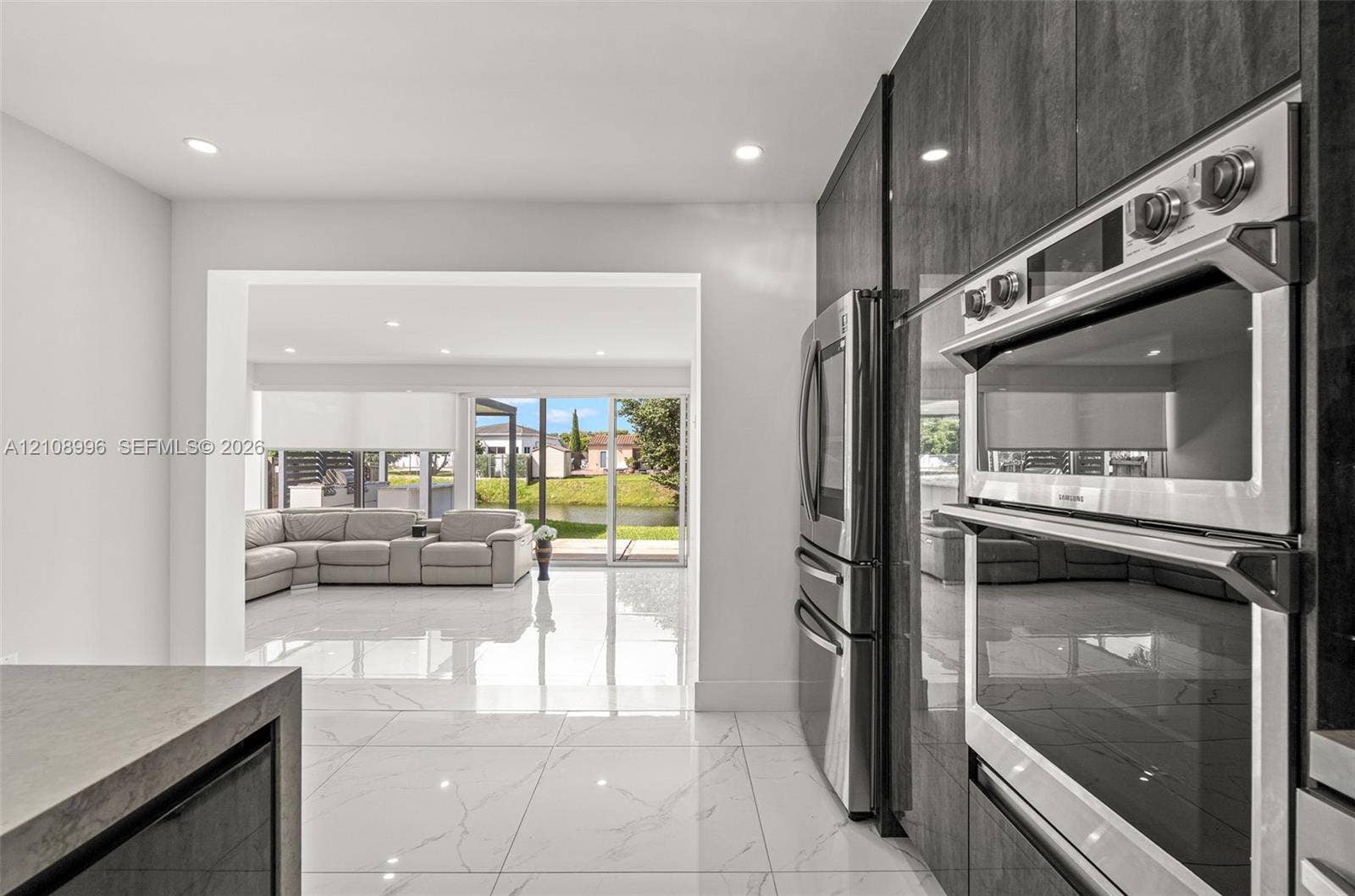 4252 SW 131st Avenue, Miami, FL 33175 Modern kitchen featuring sleek, high-gloss charcoal cabinetry, integrated stainless steel double wall ovens, a stainless steel refrigerator, and large-format porcelain tile flooring