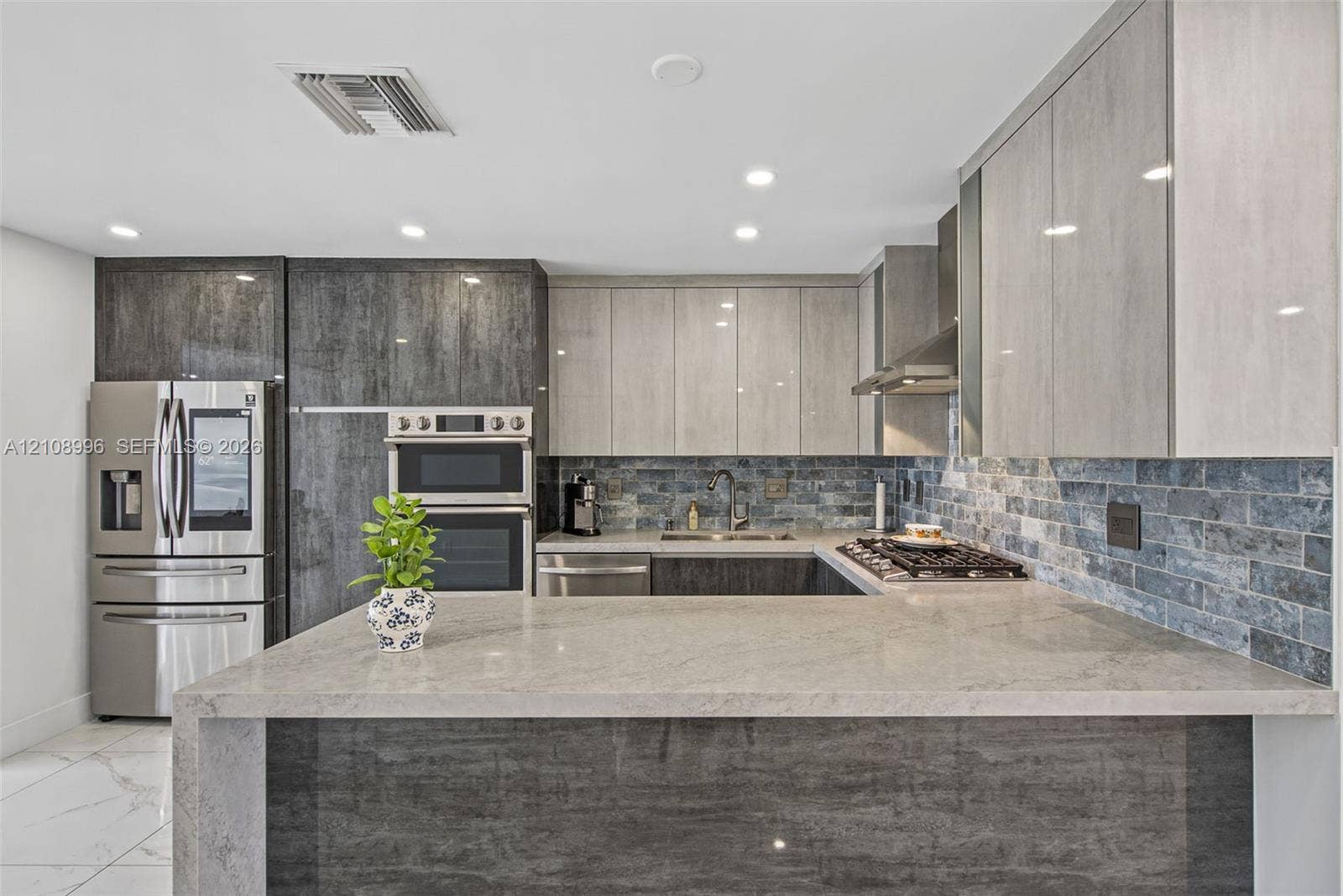 4252 SW 131st Avenue, Miami, FL 33175 Modern kitchen featuring two-tone high-gloss cabinetry, stone countertops with waterfall edge, stainless steel built-in double wall ovens, and a decorative tile backsplash