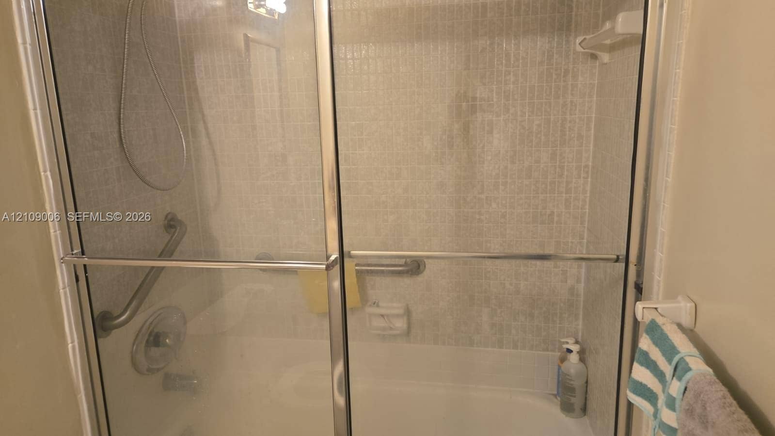 Shower and tub combination featuring sliding glass doors, a small-format tiled surround, and chrome hardware including mounted grab bars