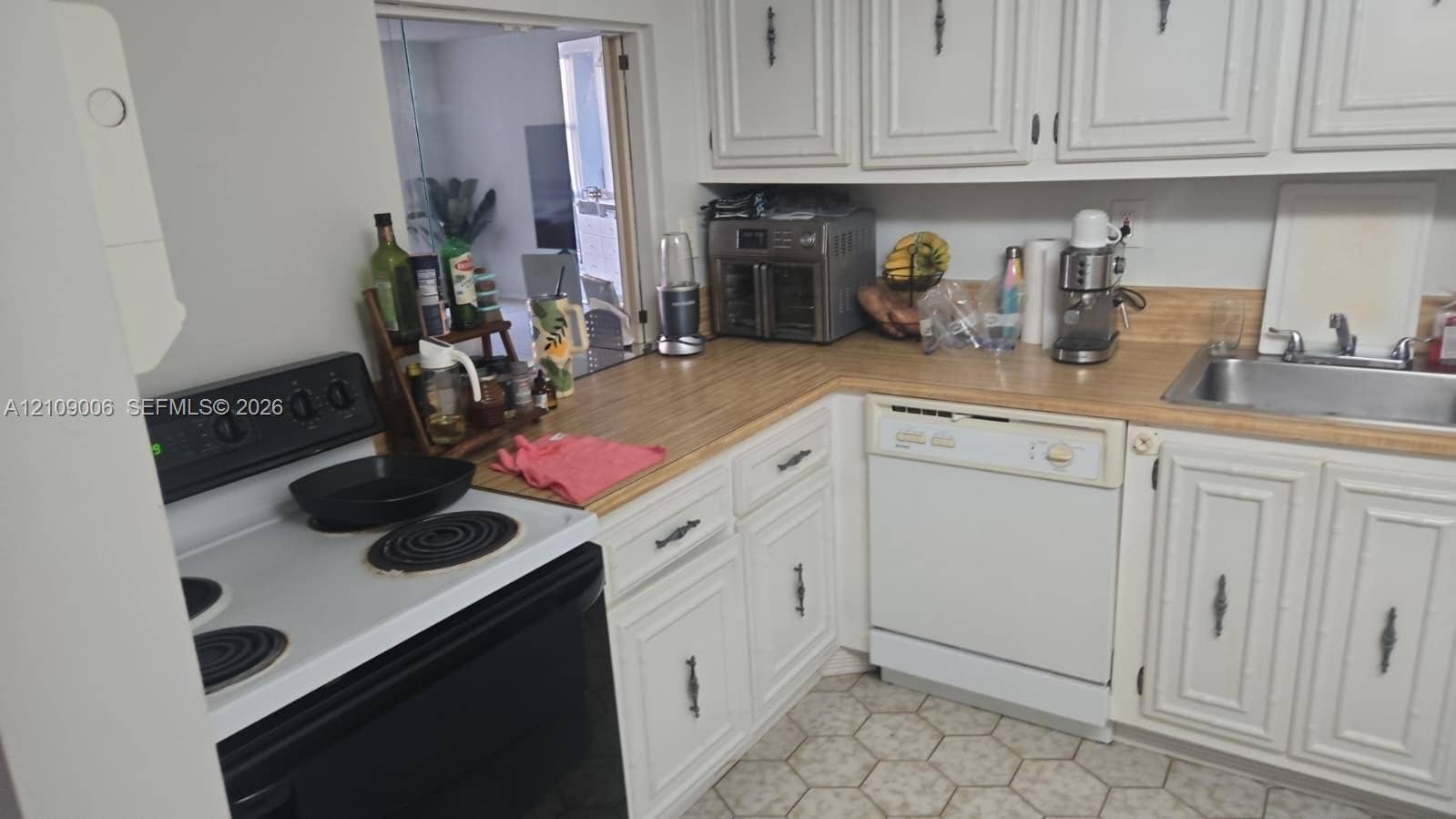 Kitchen featuring white raised-panel cabinetry, wood-finish countertops, stainless steel sink with chrome faucet, built-in dishwasher, and electric range