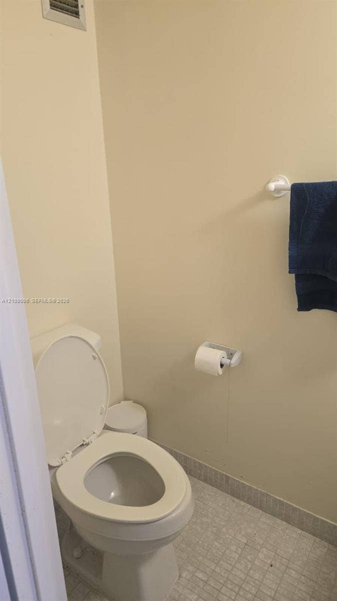 Full bathroom area featuring a white elongated toilet, tiled flooring, and wall-mounted hardware