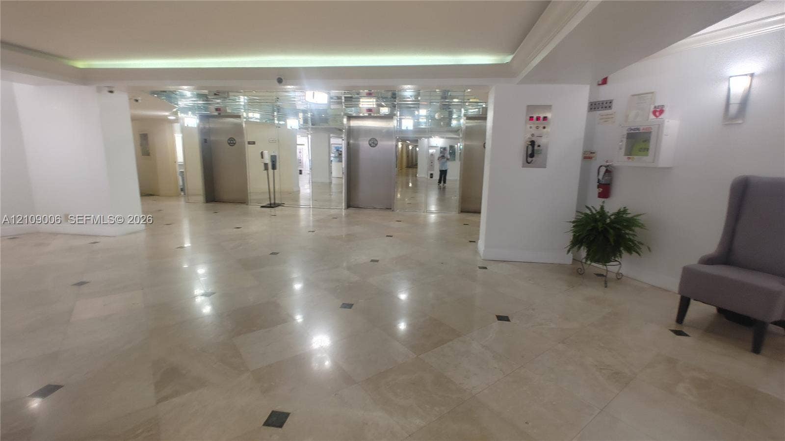 Lobby featuring polished stone flooring with inlaid tile accents, stainless steel elevator doors, mirrored wall paneling, and recessed ceiling lighting