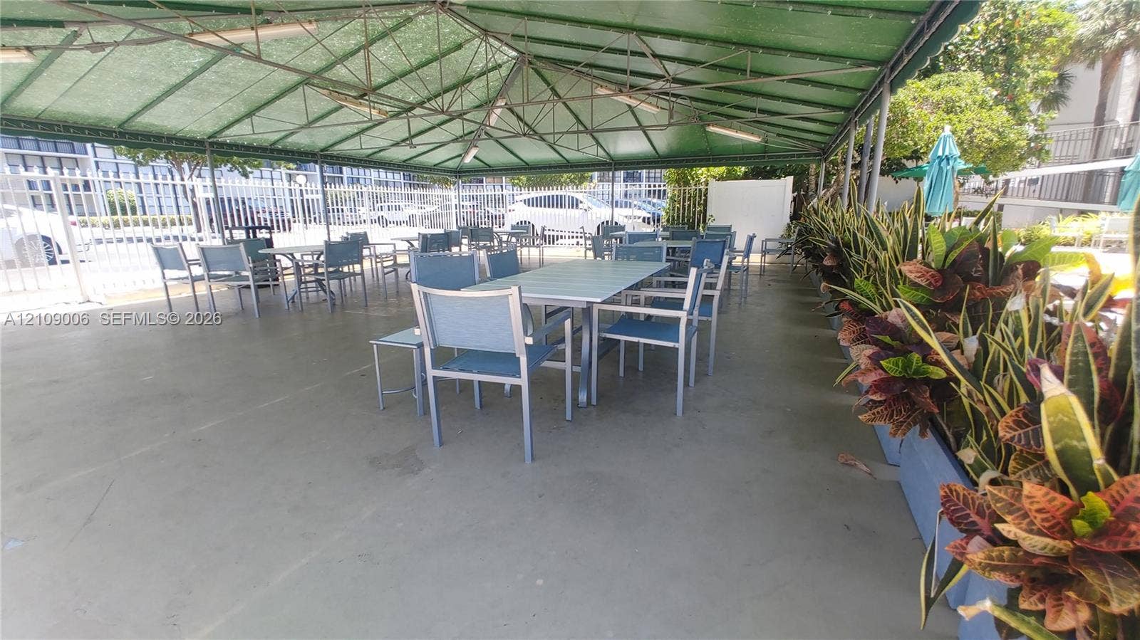 Covered outdoor patio area featuring a metal-frame canopy, smooth concrete flooring, and perimeter metal fencing