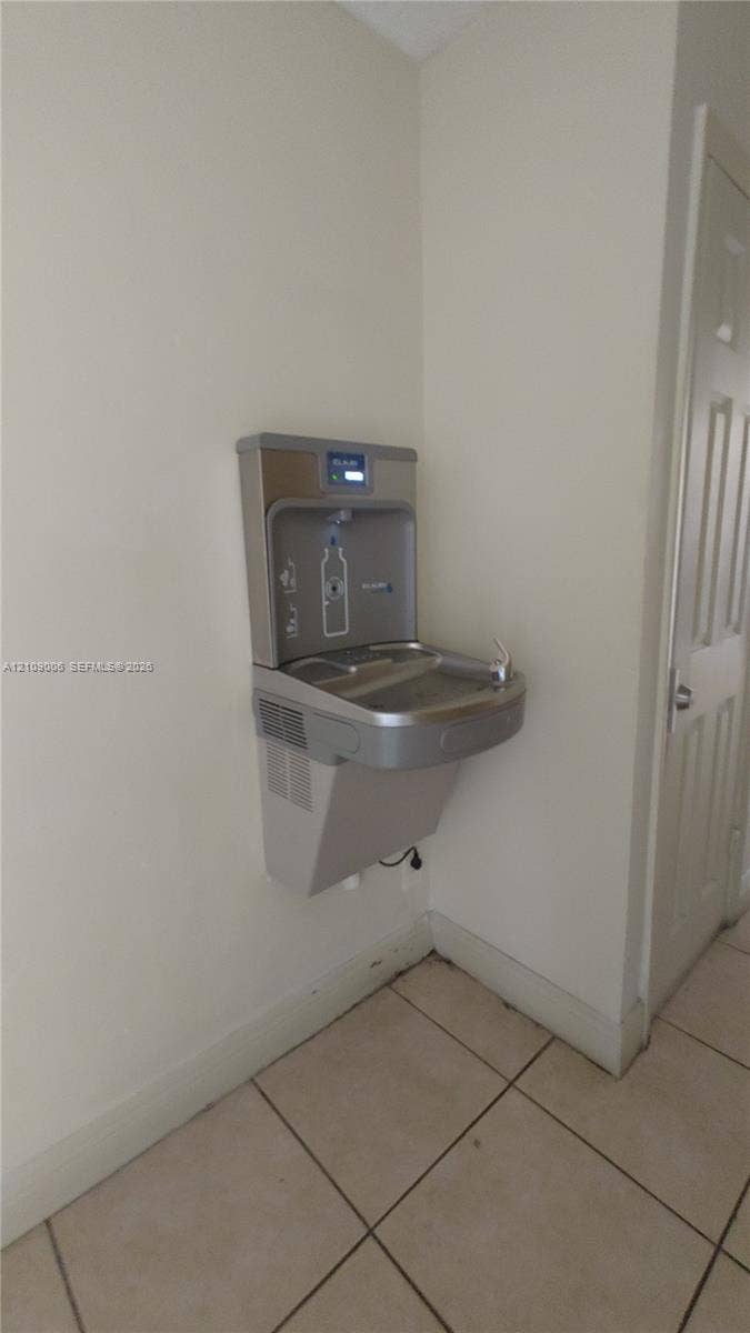 Wall-mounted stainless steel bottle filling station and water fountain with a digital filter monitor and tile flooring