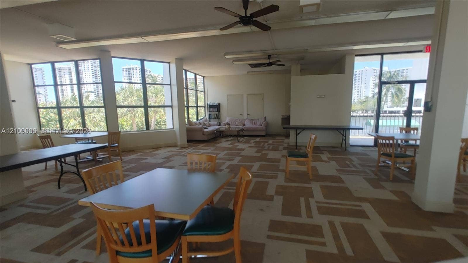 Open-concept room featuring floor-to-ceiling windows, patterned carpeting, multiple ceiling fans, and an exterior door providing outdoor access