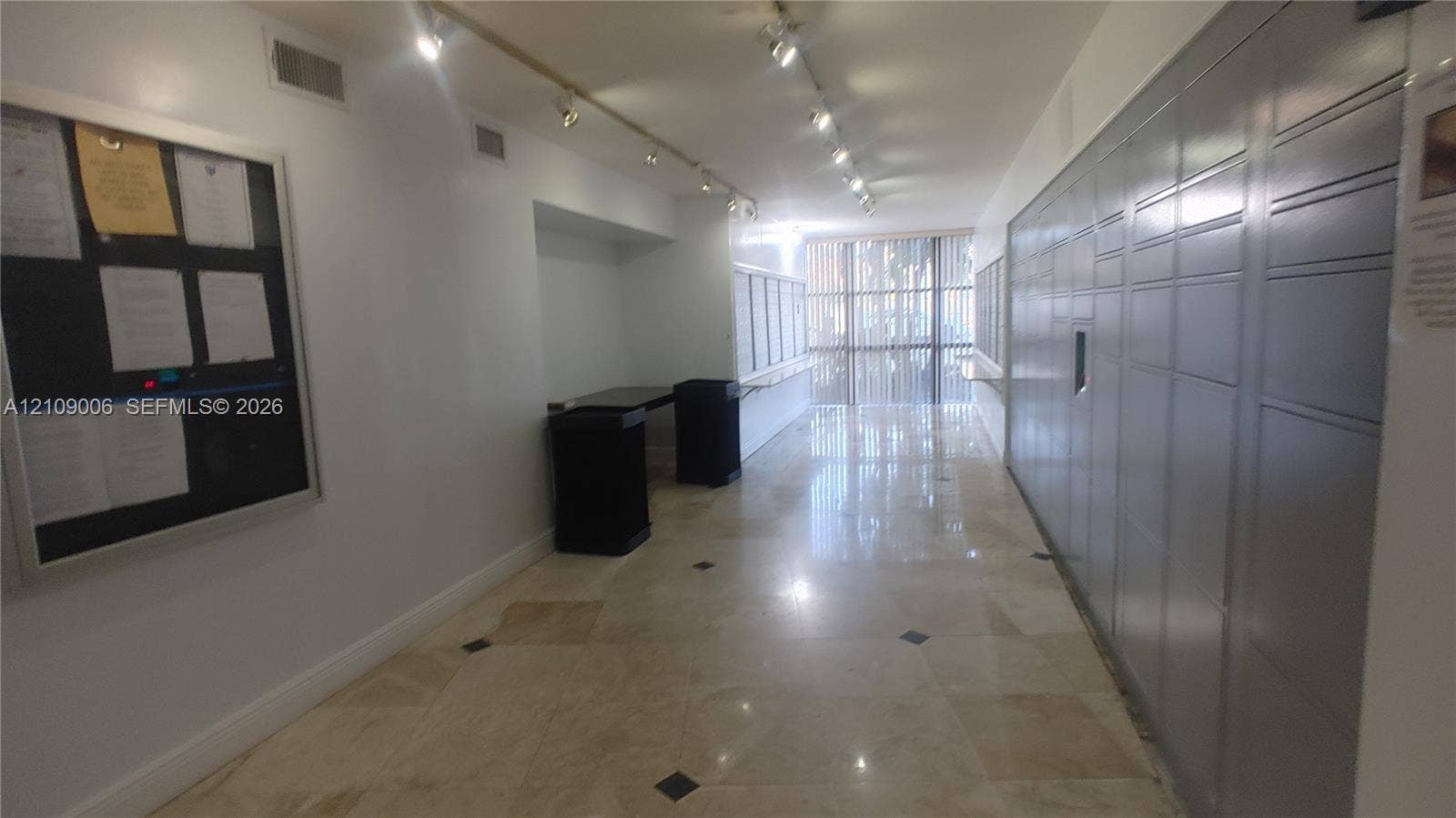 Lobby area featuring large-format tile flooring with inlaid accents, integrated package lockers, directional track lighting, and a recessed bulletin board