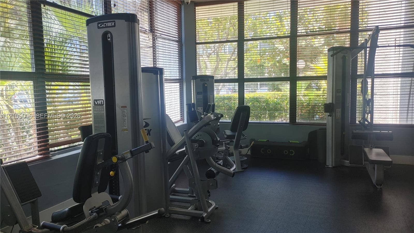 Multi-purpose fitness room featuring wall-to-wall windows, adjustable slatted blinds, and rubberized flooring