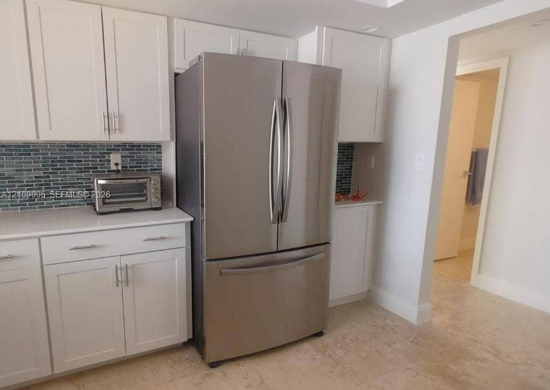 Kitchen featuring white Shaker-style cabinetry, stainless steel French door refrigerator, blue glass tile backsplash, white countertops, and stone-finish flooring