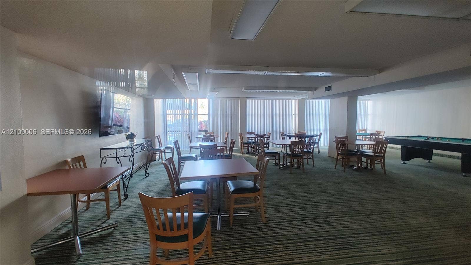 Expansive recreation area featuring floor-to-ceiling windows, wall-mounted television, and industrial-style overhead lighting