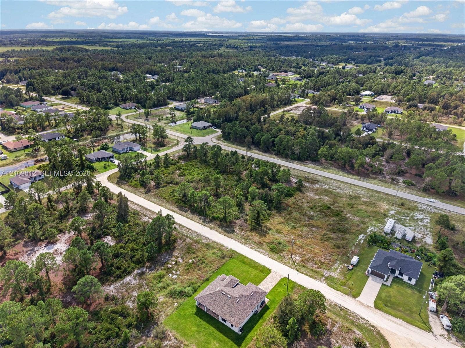 846 Burns Avenue S, Lehigh Acres, Lehigh Acres, FL 33974 Aerial perspective of a multi-lot site featuring expansive green space, mature tree lines, and paved access roads