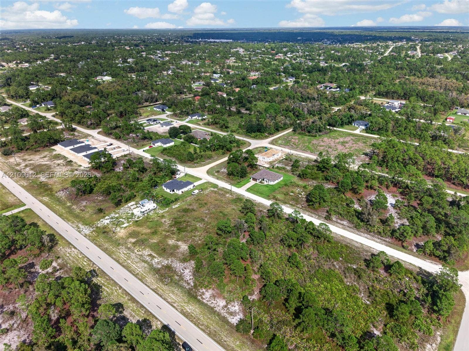 846 Burns Avenue S, Lehigh Acres, Lehigh Acres, FL 33974 Aerial perspective featuring expansive undeveloped land parcel, paved road access, and surrounding native vegetation