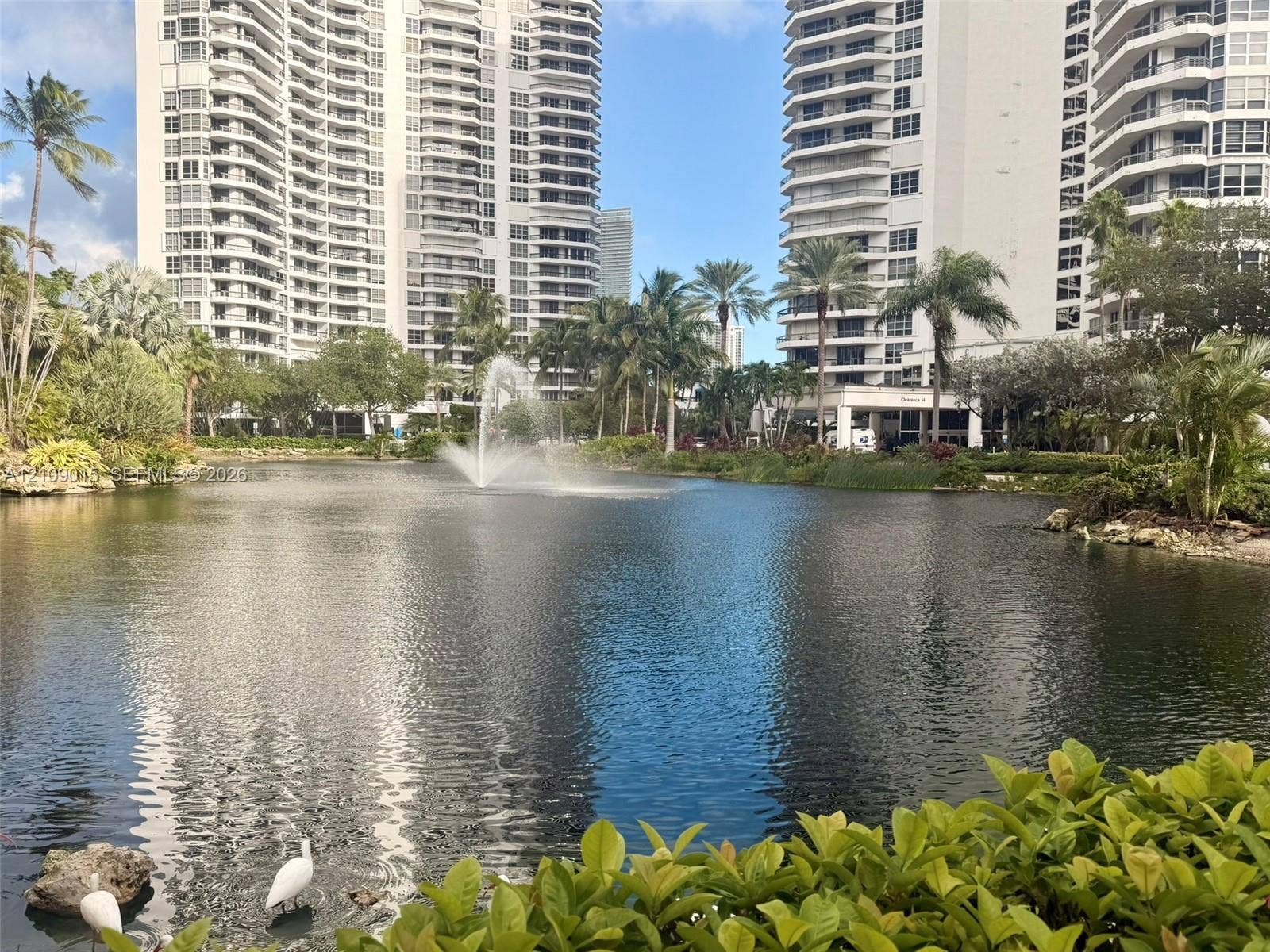 3530 Mystic Pointe Drive, #1709, Aventura, FL 33180 Serene pond featuring a central fountain, lush tropical landscaping, and mature palm trees