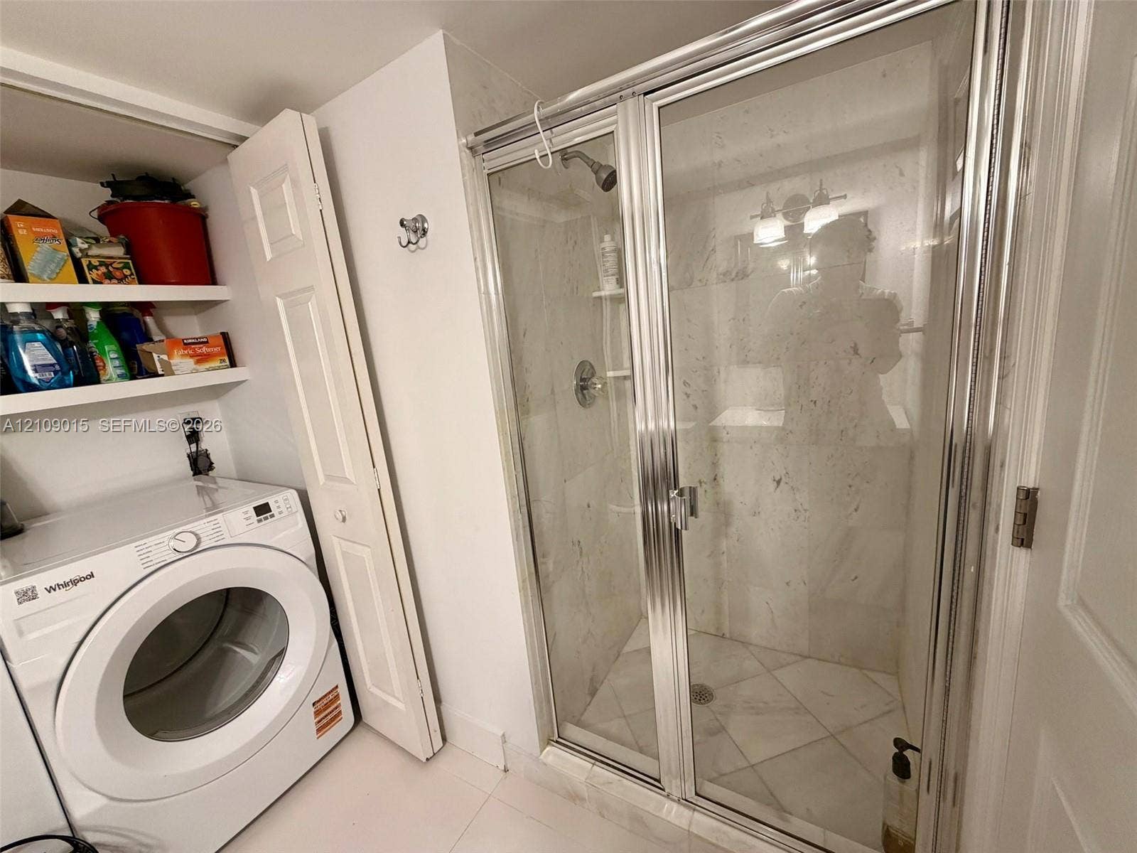 3530 Mystic Pointe Drive, #1709, Aventura, FL 33180 Walk-in shower enclosure with glass doors, stone-finish wall tiling, built-in shelving, chrome-finish plumbing fixtures, and integrated laundry area with overhead storage shelving