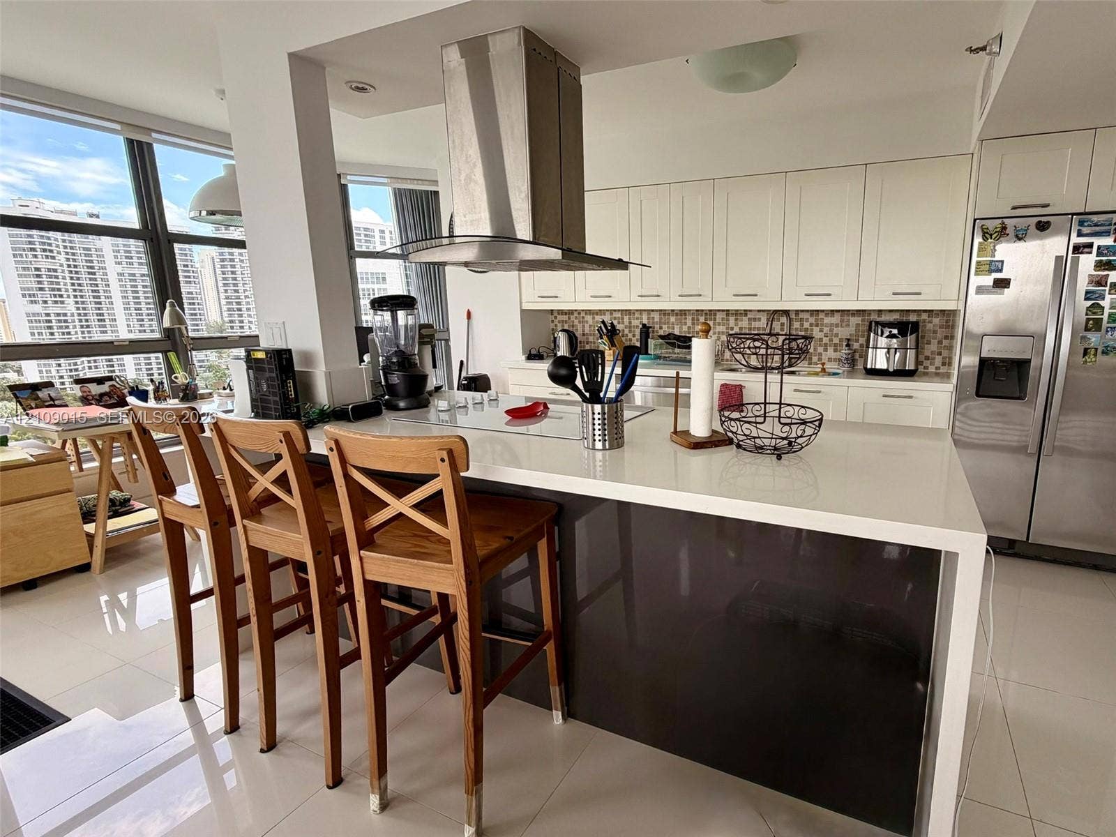 3530 Mystic Pointe Drive, #1709, Aventura, FL 33180 Kitchen featuring an island with a solid-surface countertop, stainless steel chimney-style range hood, white shaker-style cabinetry, mosaic tile backsplash, and floor-to-ceiling windows