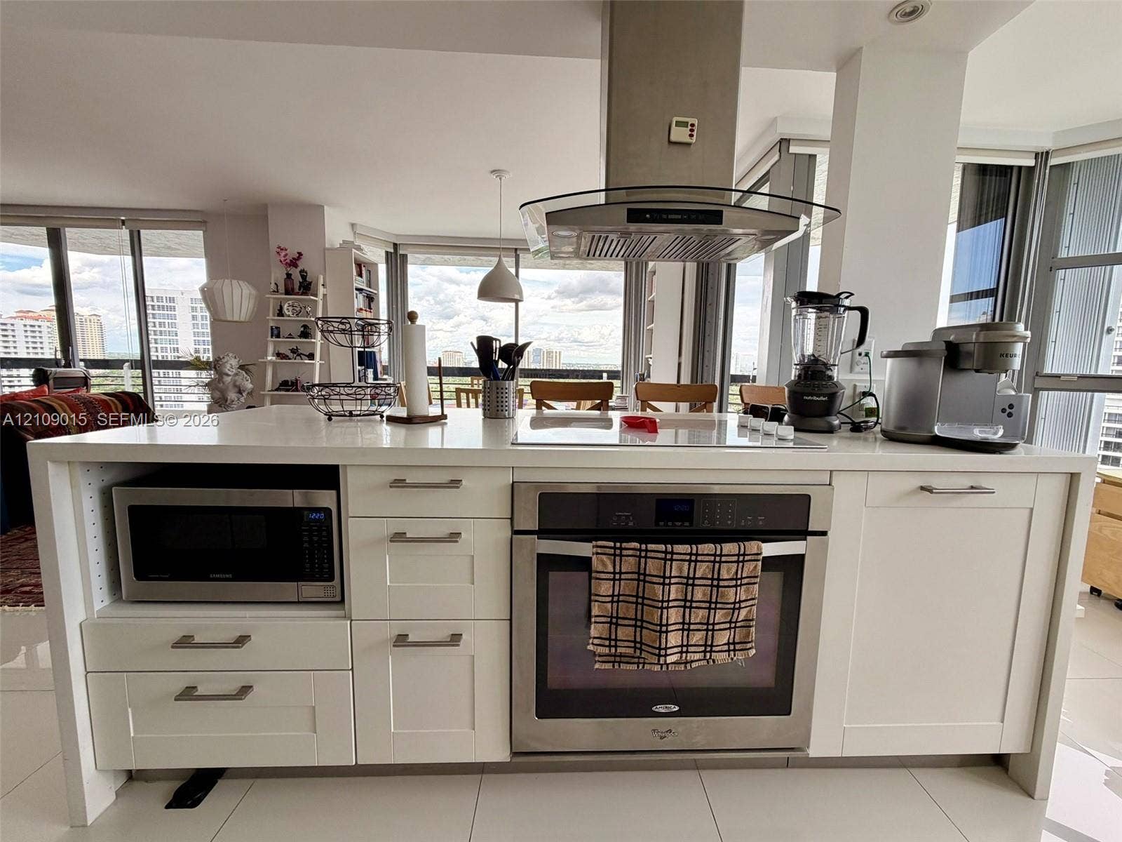 3530 Mystic Pointe Drive, #1709, Aventura, FL 33180 Kitchen island featuring white cabinetry, a light-toned solid surface countertop, stainless steel oven, integrated microwave, and an overhead stainless steel range hood