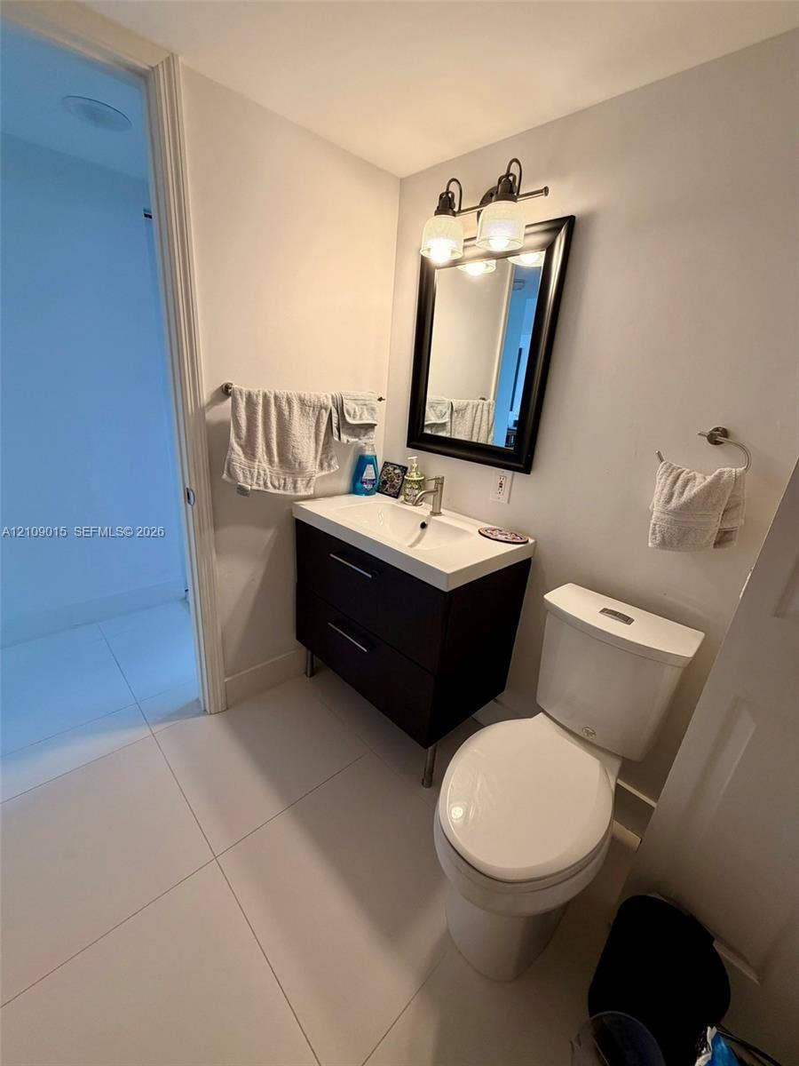3530 Mystic Pointe Drive, #1709, Aventura, FL 33180 Modern floating vanity featuring two drawers, a white integrated basin, and a wall-mounted light fixture, paired with a white-framed mirror and ceramic tile flooring