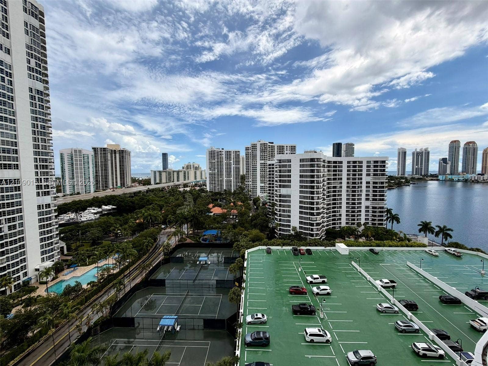 3530 Mystic Pointe Drive, #1709, Aventura, FL 33180 High-rise perspective featuring tennis courts, a surface parking structure, and proximity to an expansive waterfront canal and urban skyline