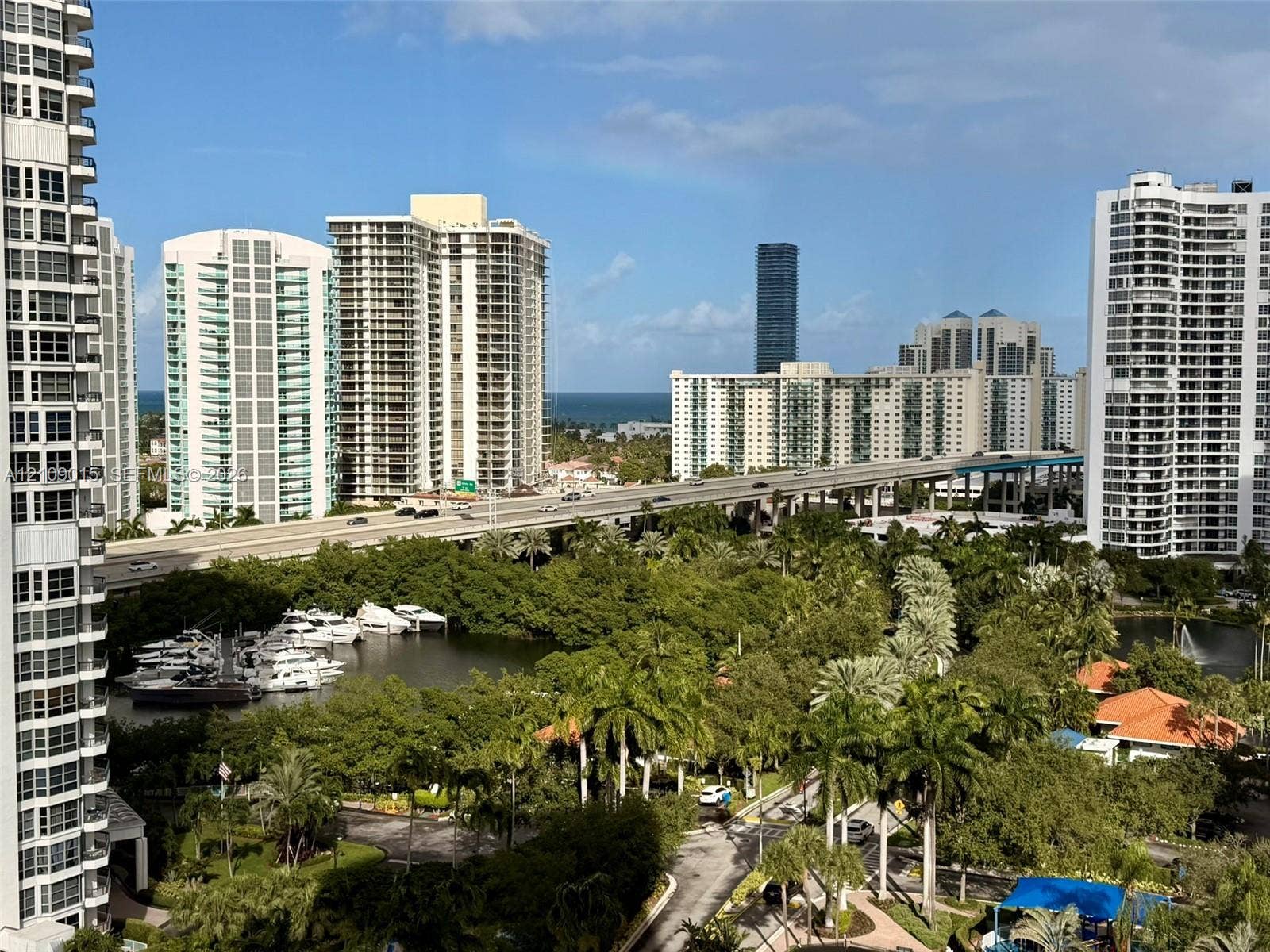 3530 Mystic Pointe Drive, #1709, Aventura, FL 33180 Panoramic cityscape featuring high-rise architecture, a coastal waterway with boat docks, lush palm trees, and an ocean horizon