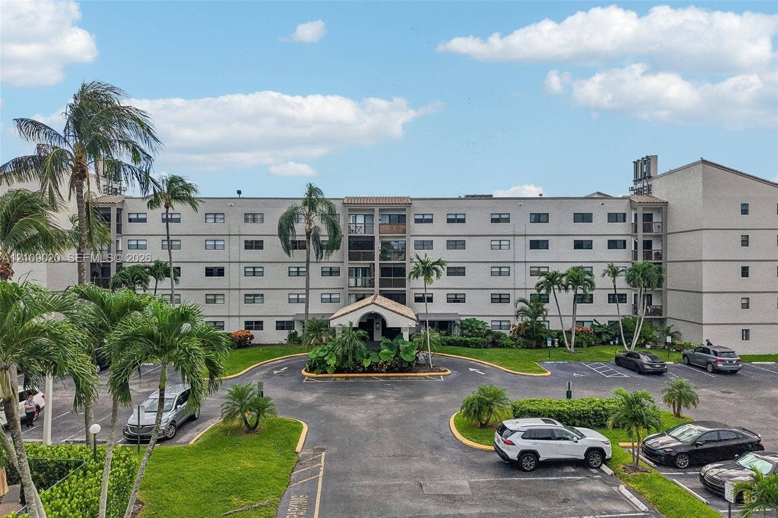 701 NW 19th Street, #300, Fort Lauderdale, FL 33311 Multi-story residential building featuring a covered entryway, paved surface parking, and mature palm landscaping
