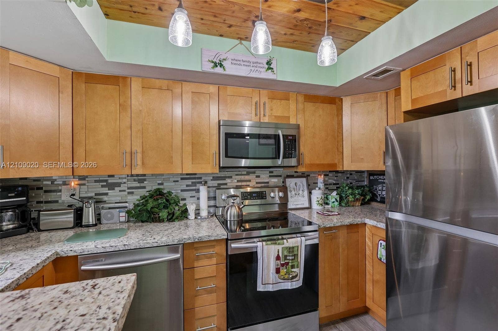 701 NW 19th Street, #300, Fort Lauderdale, FL 33311 Kitchen featuring shaker-style wood cabinetry, stainless steel appliances, speckled stone countertops, a multi-tonal tile backsplash, and a wood-plank ceiling with pendant lighting