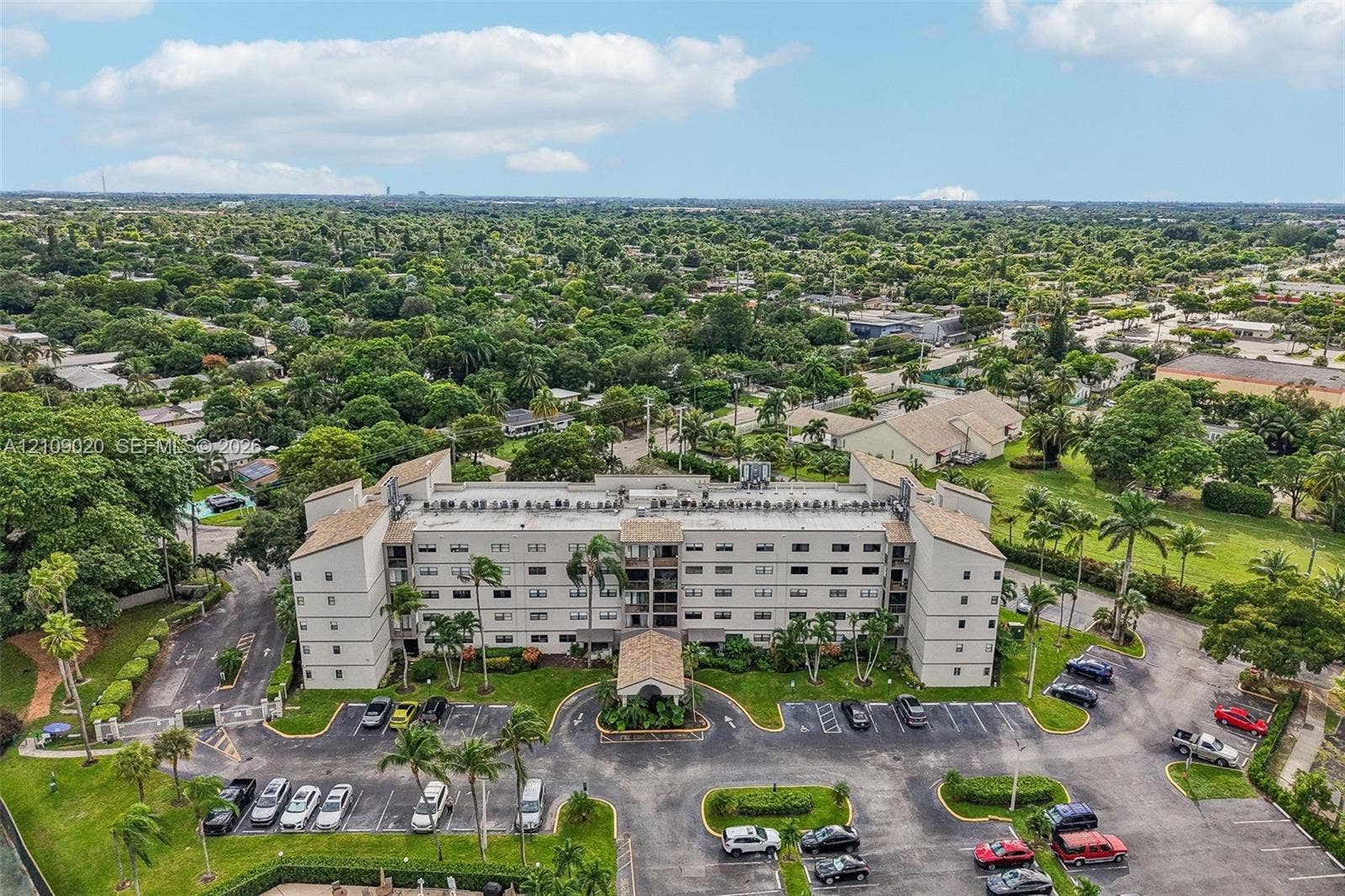 701 NW 19th Street, #300, Fort Lauderdale, FL 33311 Multi-story residential building featuring a covered entryway, paved surface parking, and manicured landscaping with mature palm trees