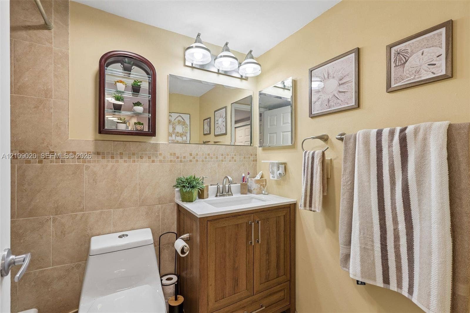 701 NW 19th Street, #300, Fort Lauderdale, FL 33311 Bathroom featuring a wood-finish vanity with an integrated rectangular sink, stone-tile wainscoting with mosaic accent detailing, a triple-light vanity fixture, and a wall-mounted mirror