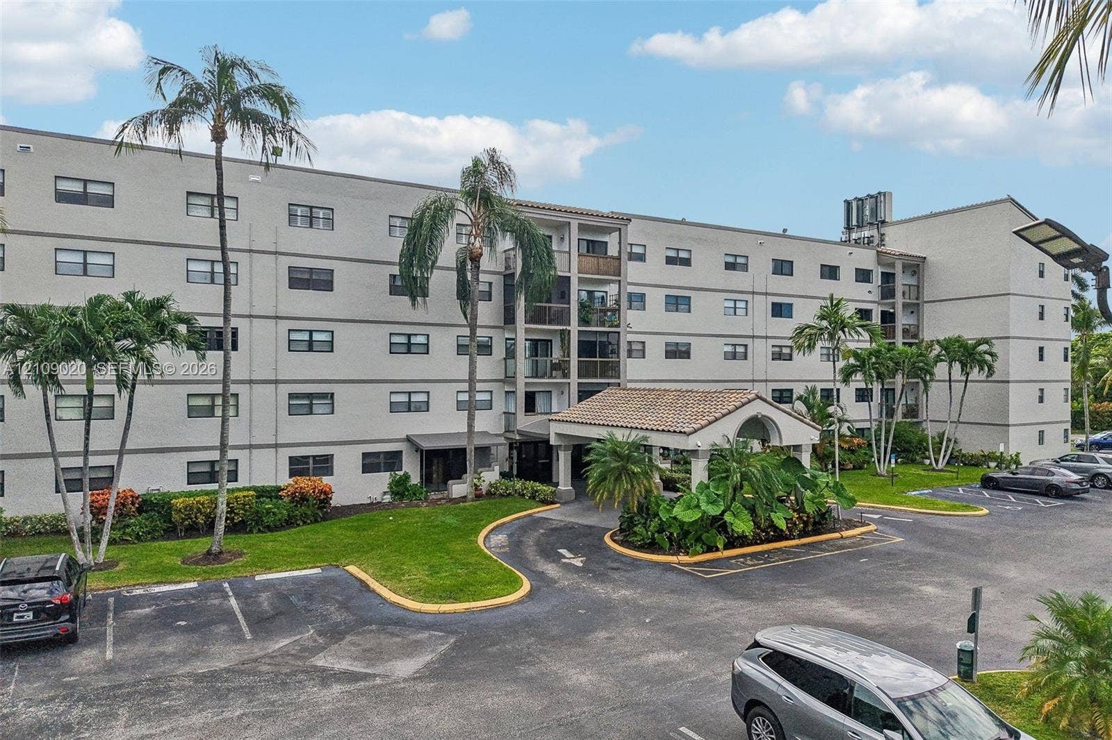 701 NW 19th Street, #300, Fort Lauderdale, FL 33311 Multi-story residential building featuring a covered portico entrance with clay tile roofing, manicured green space, and palm tree landscaping