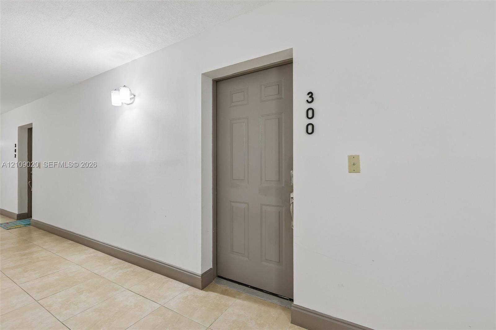701 NW 19th Street, #300, Fort Lauderdale, FL 33311 Six-panel entry door with polished hardware, neutral tile flooring, and wall-mounted light fixture