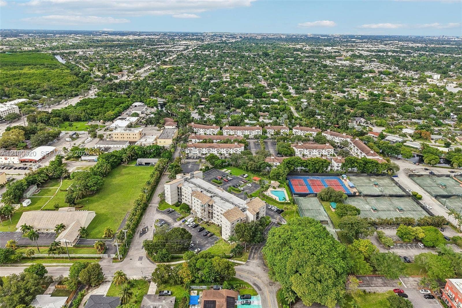701 NW 19th Street, #300, Fort Lauderdale, FL 33311 Aerial perspective of a multi-story residential complex featuring multiple outdoor tennis courts, a swimming pool, and paved surface parking