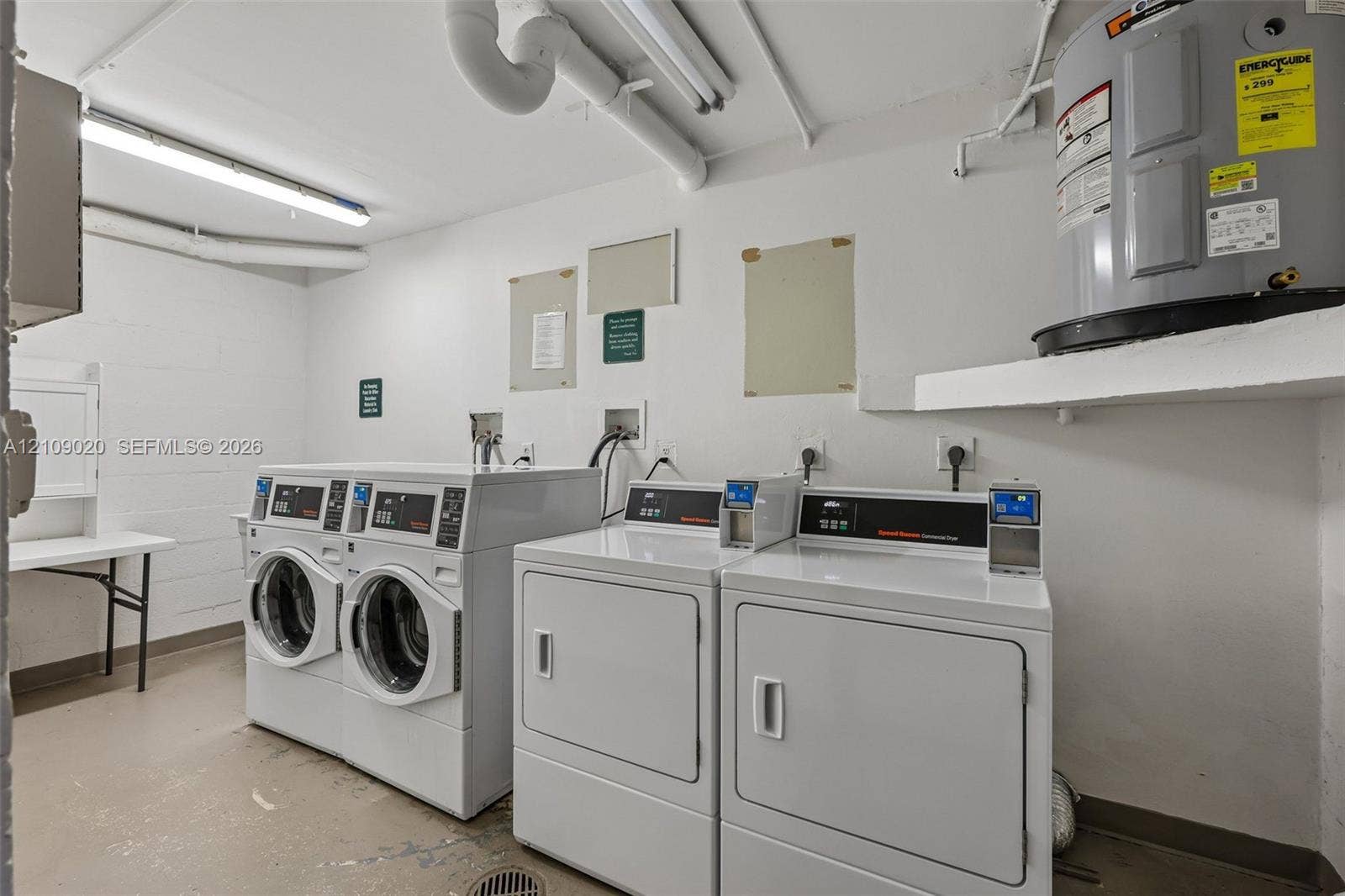 701 NW 19th Street, #300, Fort Lauderdale, FL 33311 Utility space featuring two front-loading washers, two commercial-grade dryers, wall-mounted water heater, and fluorescent lighting