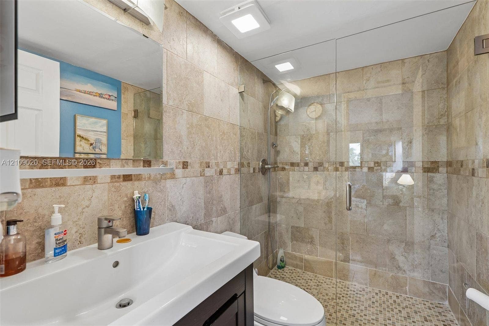 701 NW 19th Street, #300, Fort Lauderdale, FL 33311 Bathroom featuring large-format natural stone wall tiling with mosaic accent banding, a glass-enclosed shower with pebble tile flooring, and a dark-finish vanity with an integrated basin