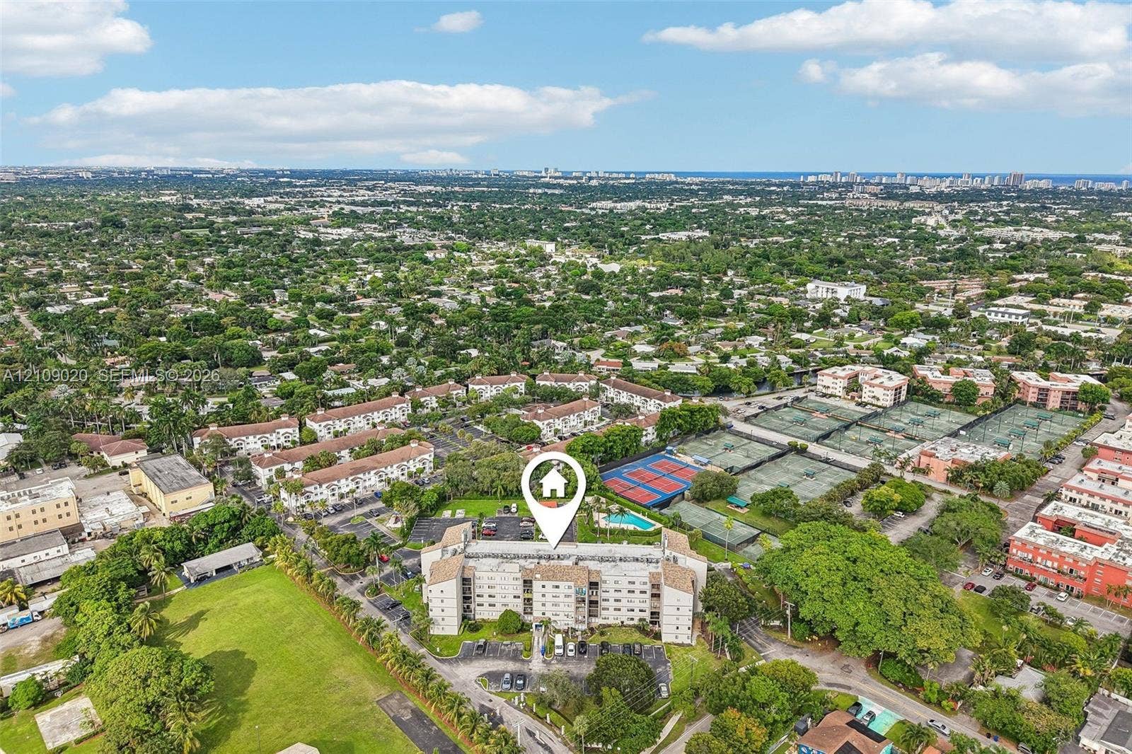 701 NW 19th Street, #300, Fort Lauderdale, FL 33311 Aerial perspective of a multi-story residential building featuring on-site tennis courts, a community pool, surface parking, and extensive mature landscaping