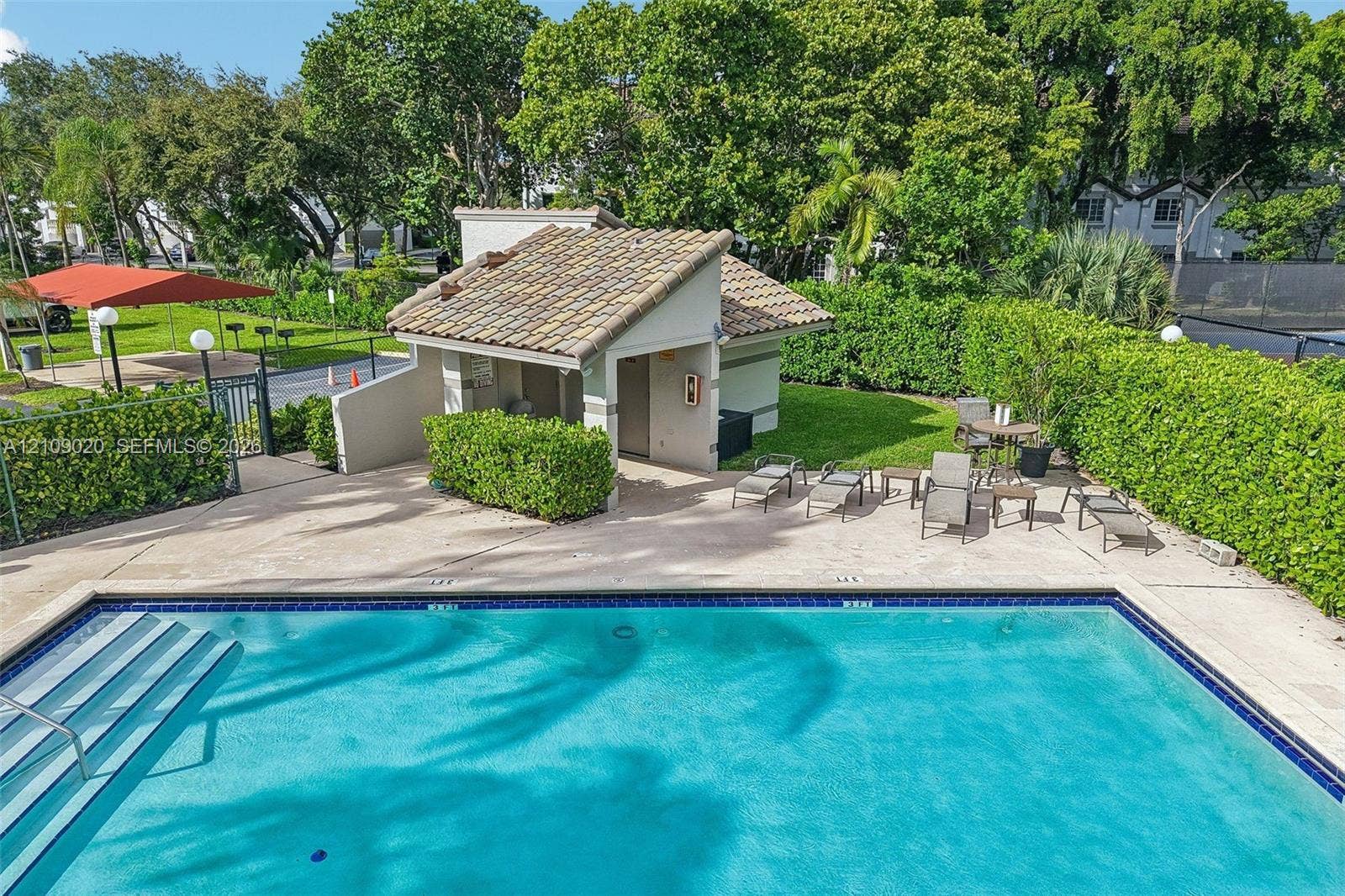701 NW 19th Street, #300, Fort Lauderdale, FL 33311 Swimming pool with tile edging and built-in stairs, concrete pool deck, tile-roofed cabana, and manicured perimeter hedges