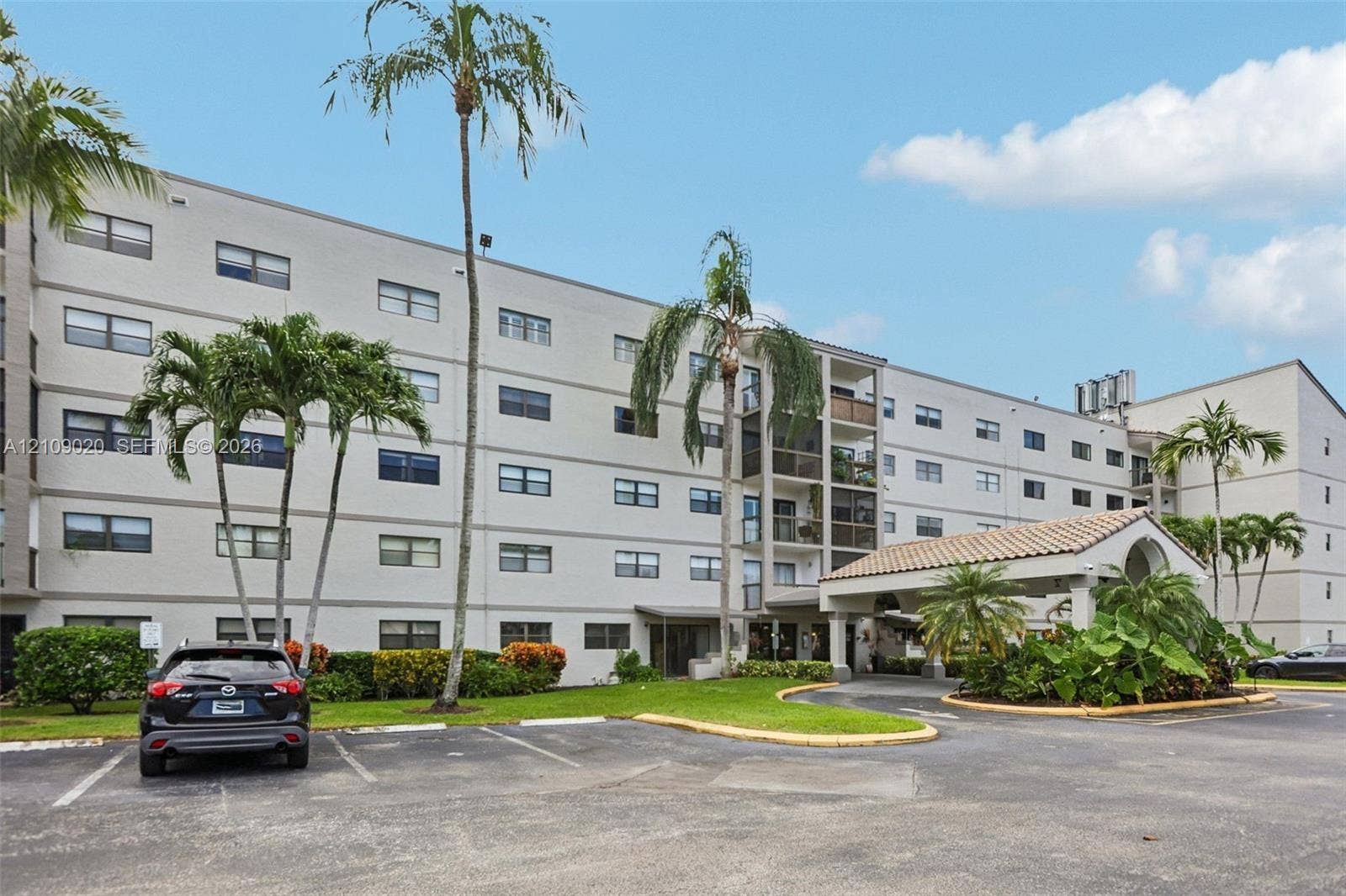 701 NW 19th Street, #300, Fort Lauderdale, FL 33311 Multi-story residential building exterior featuring a covered porte-cochre, tiled roof detailing, and established palm trees