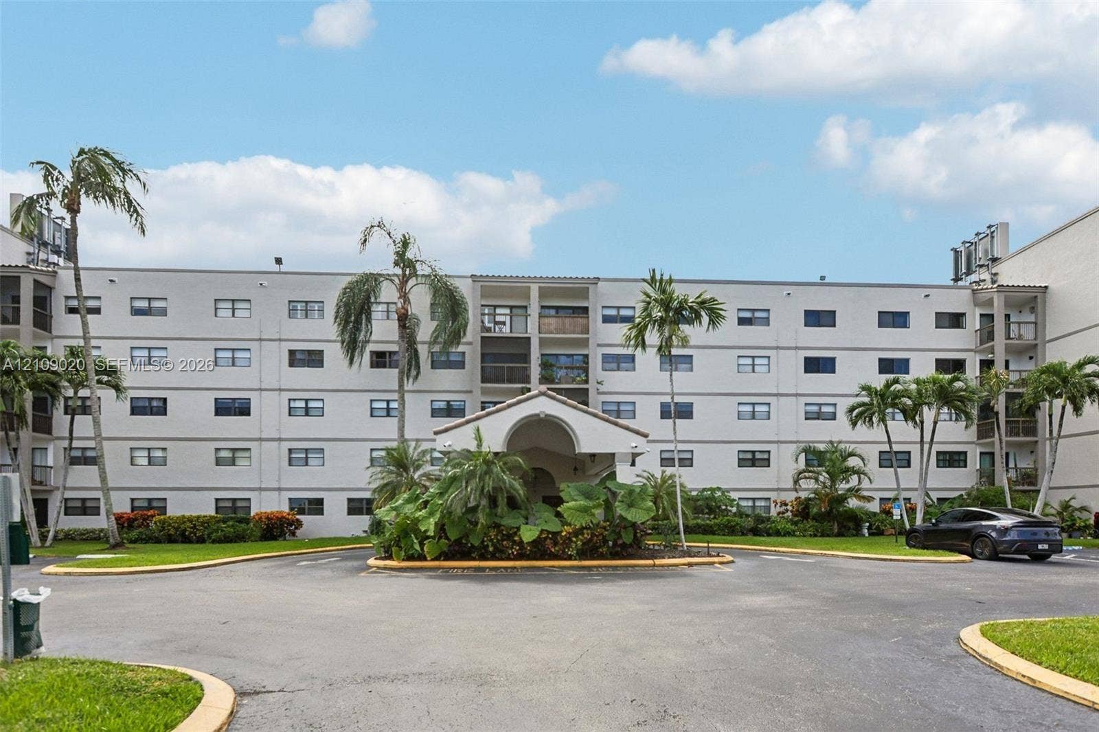 701 NW 19th Street, #300, Fort Lauderdale, FL 33311 Multi-story stucco exterior featuring a covered entryway, private balconies, and landscaped grounds with mature palm trees