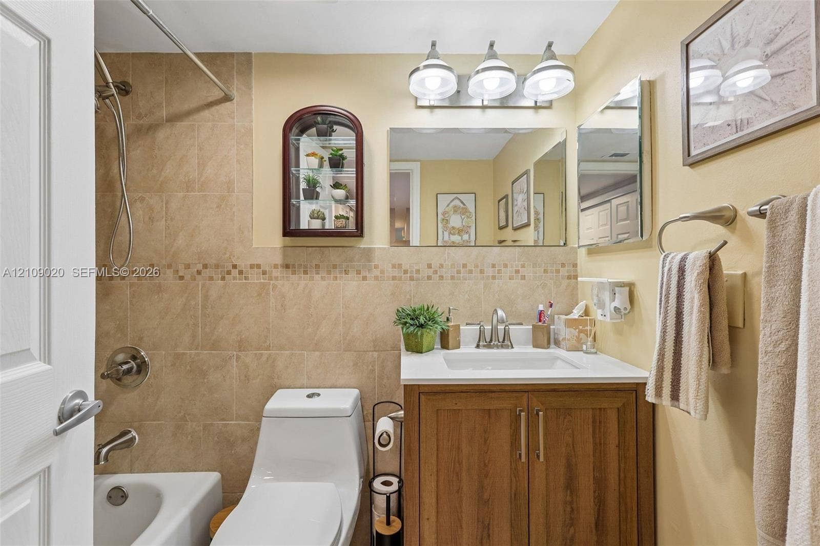 701 NW 19th Street, #300, Fort Lauderdale, FL 33311 Bathroom featuring a wood-finish vanity with a white countertop, wall-mounted mirrored medicine cabinet, three-light fixture, and a tiled shower surround