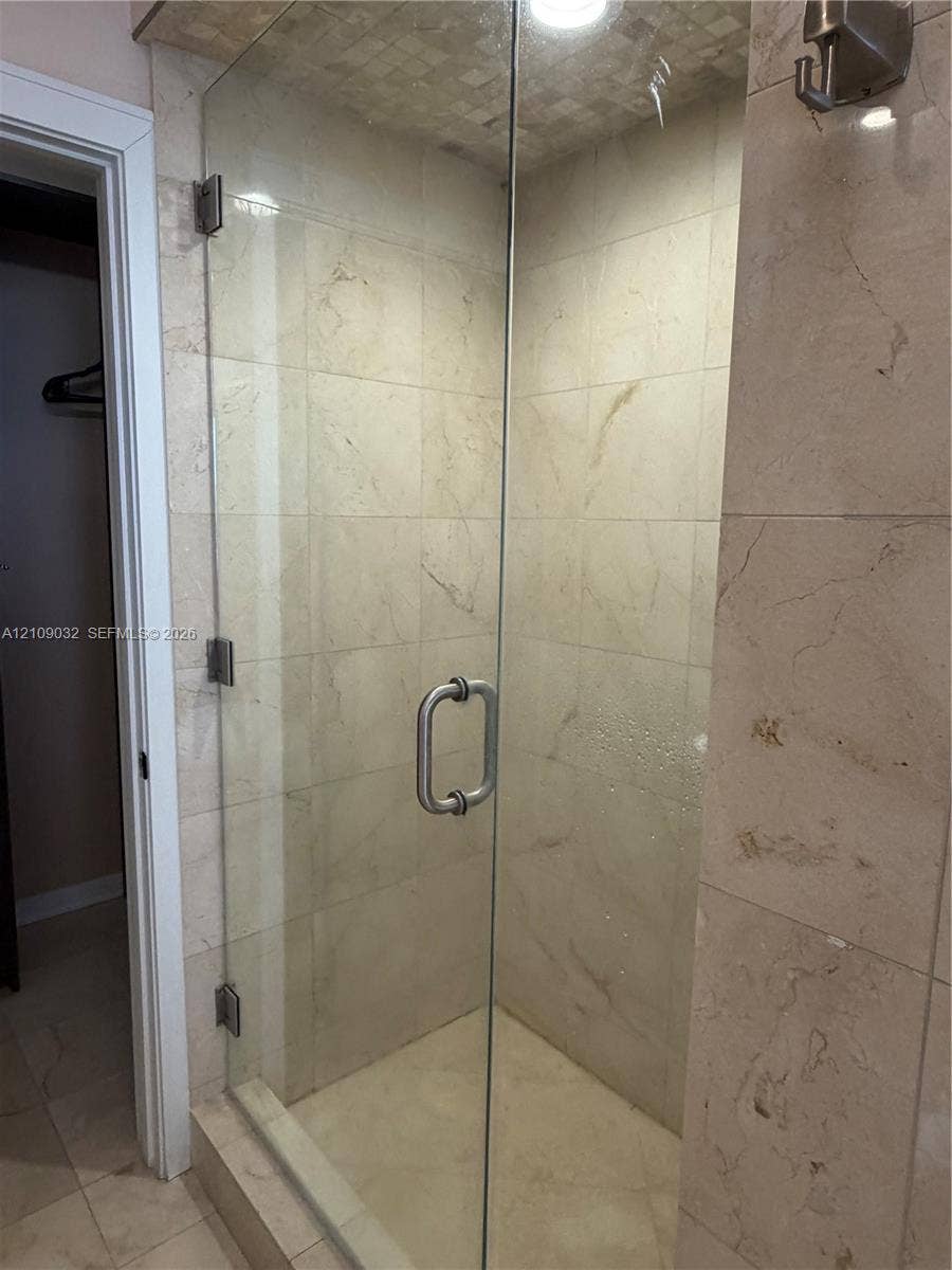 Walk-in shower featuring large-format neutral stone tiling, floor-to-ceiling glass enclosure, brushed metal hardware, and a mosaic tile ceiling accent
