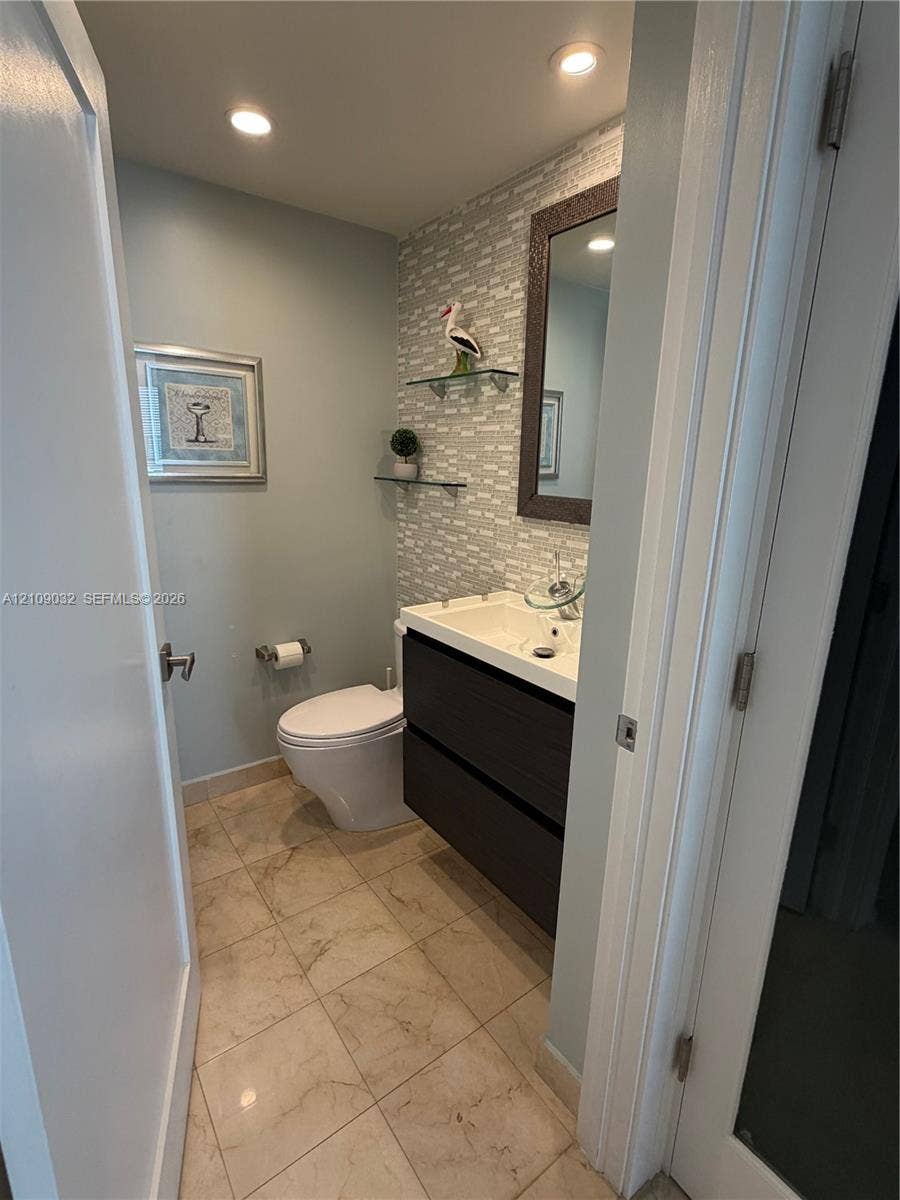 Floating vanity with dual soft-close drawers, stone-finish floor tiling, textured wall tile backsplash, integrated glass shelving, and recessed lighting