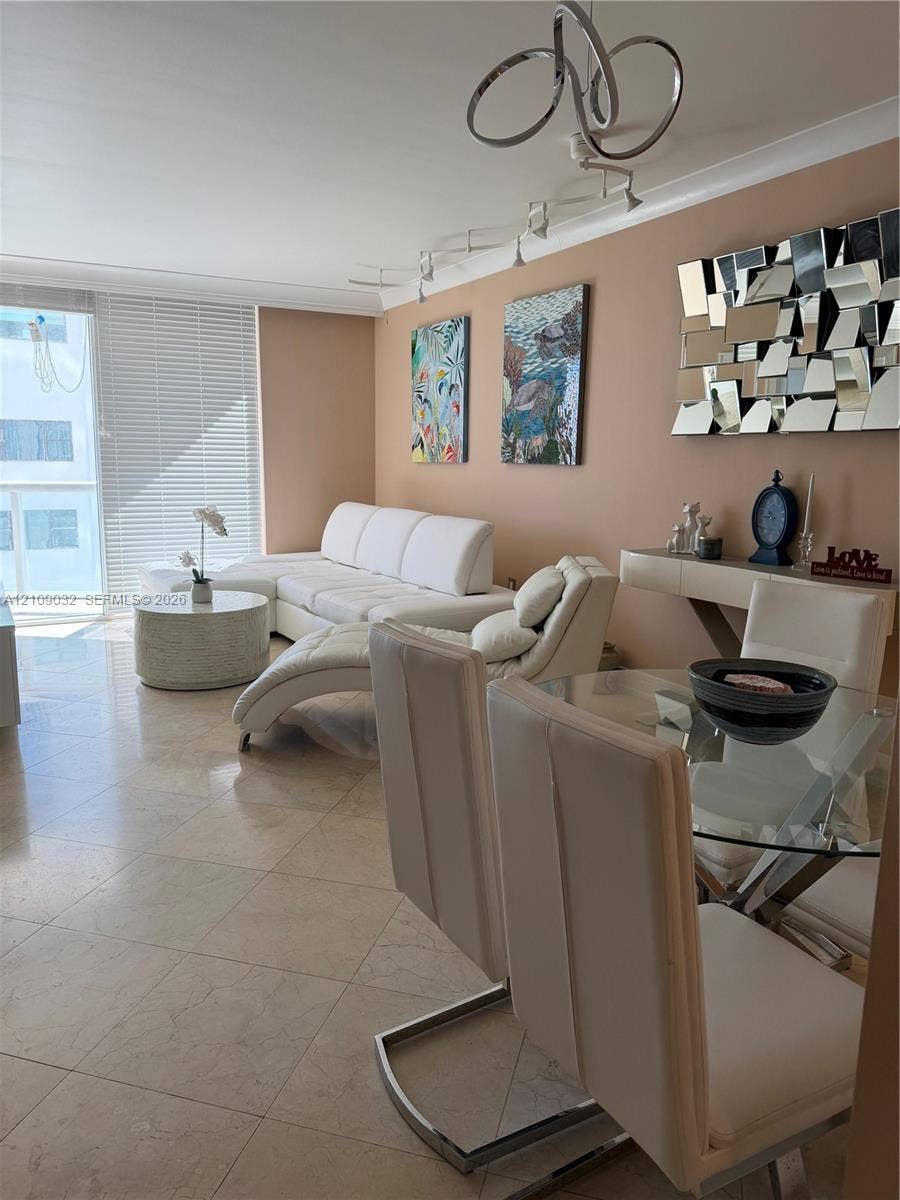 Neutral-toned living space featuring large-format tile flooring, a modern multi-ring ceiling fixture, integrated track lighting, and floor-to-ceiling glass sliding doors with horizontal blinds