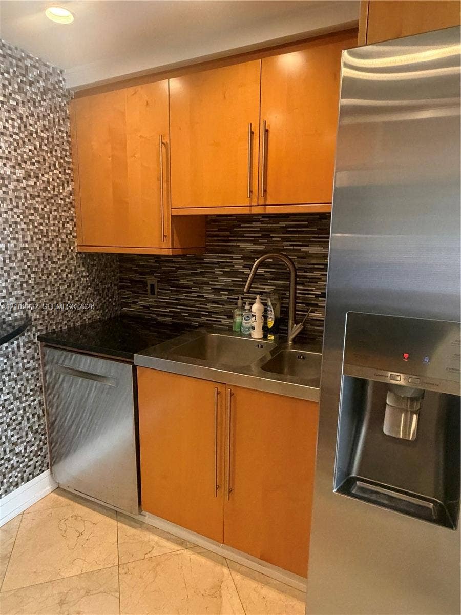 Kitchen area featuring wood cabinetry, stainless steel appliances, a stone-finish tile backsplash, and a double-basin stainless steel sink