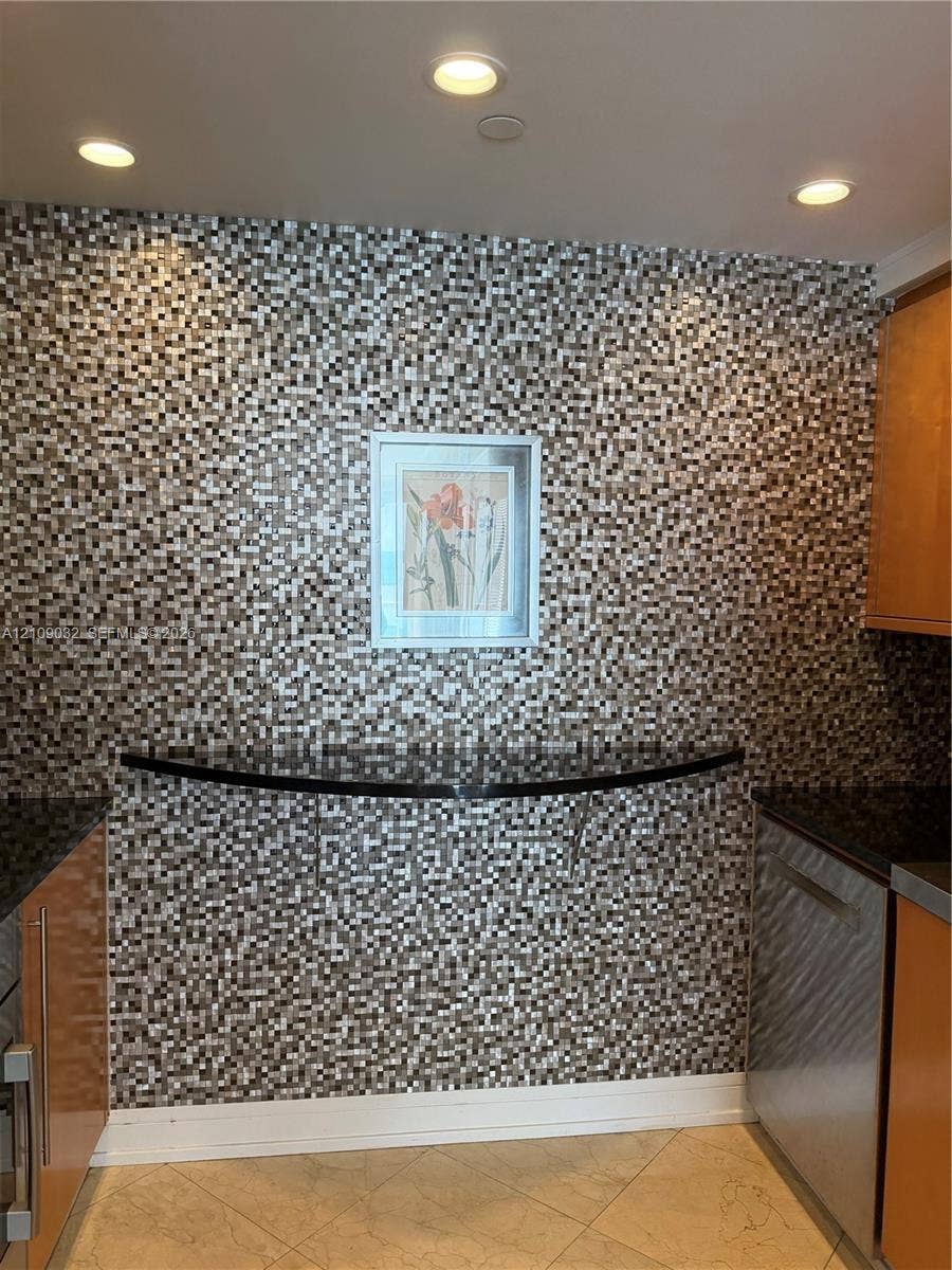 Mosaic tile accent wall featuring a curved stone-finish ledge, flat-panel cabinetry, stainless steel appliances, and recessed lighting