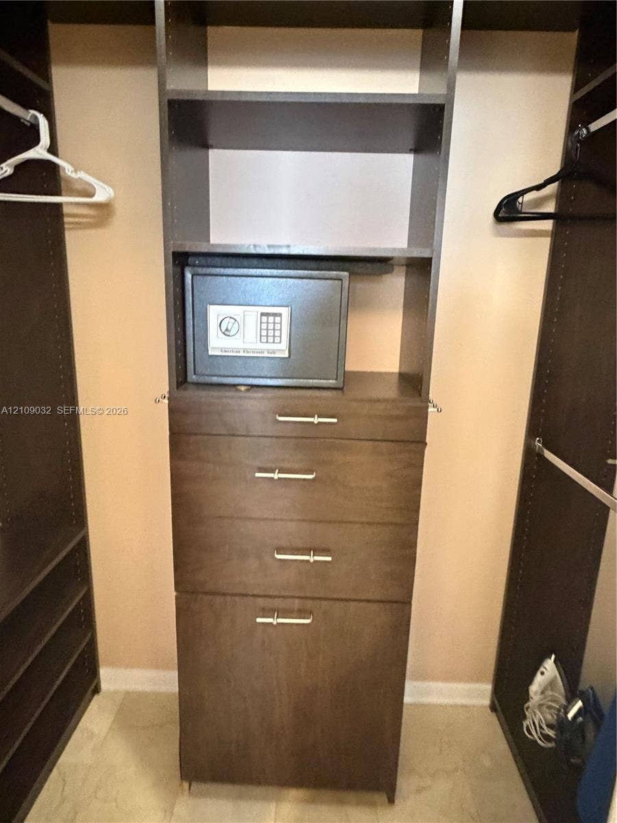 Custom walk-in closet featuring dark wood-finish cabinetry, built-in shelving, three integrated drawers with metallic pulls, and a built-in wall safe