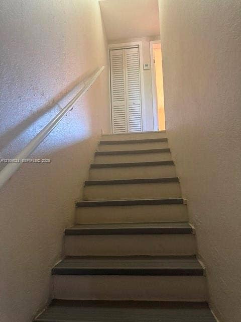 Staircase featuring painted risers and treads with a wall-mounted handrail and bi-fold closet door