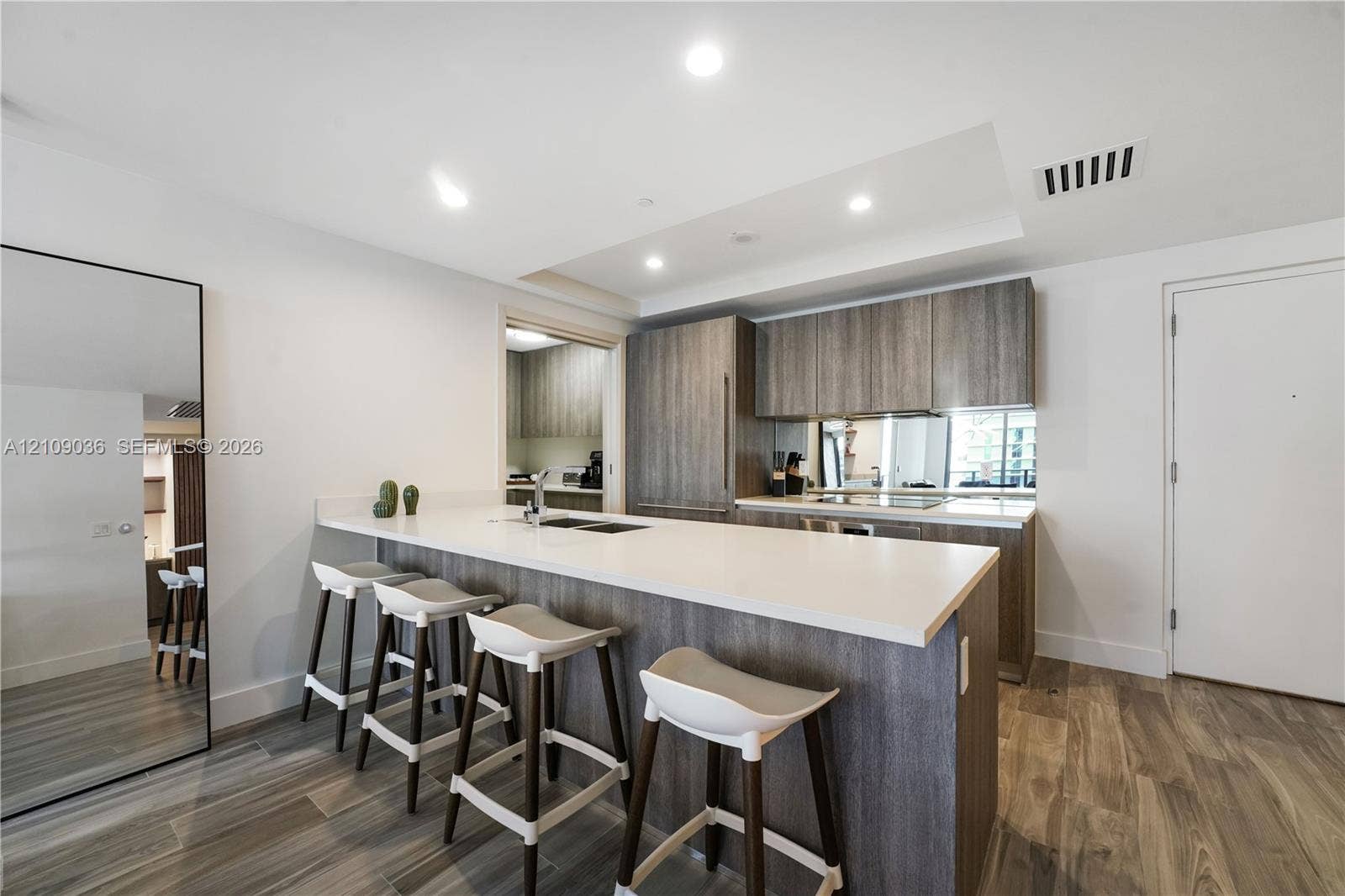 Kitchen featuring a white countertop island with an integrated sink, wood-finish cabinetry, recessed ceiling lighting, and wood-finish flooring