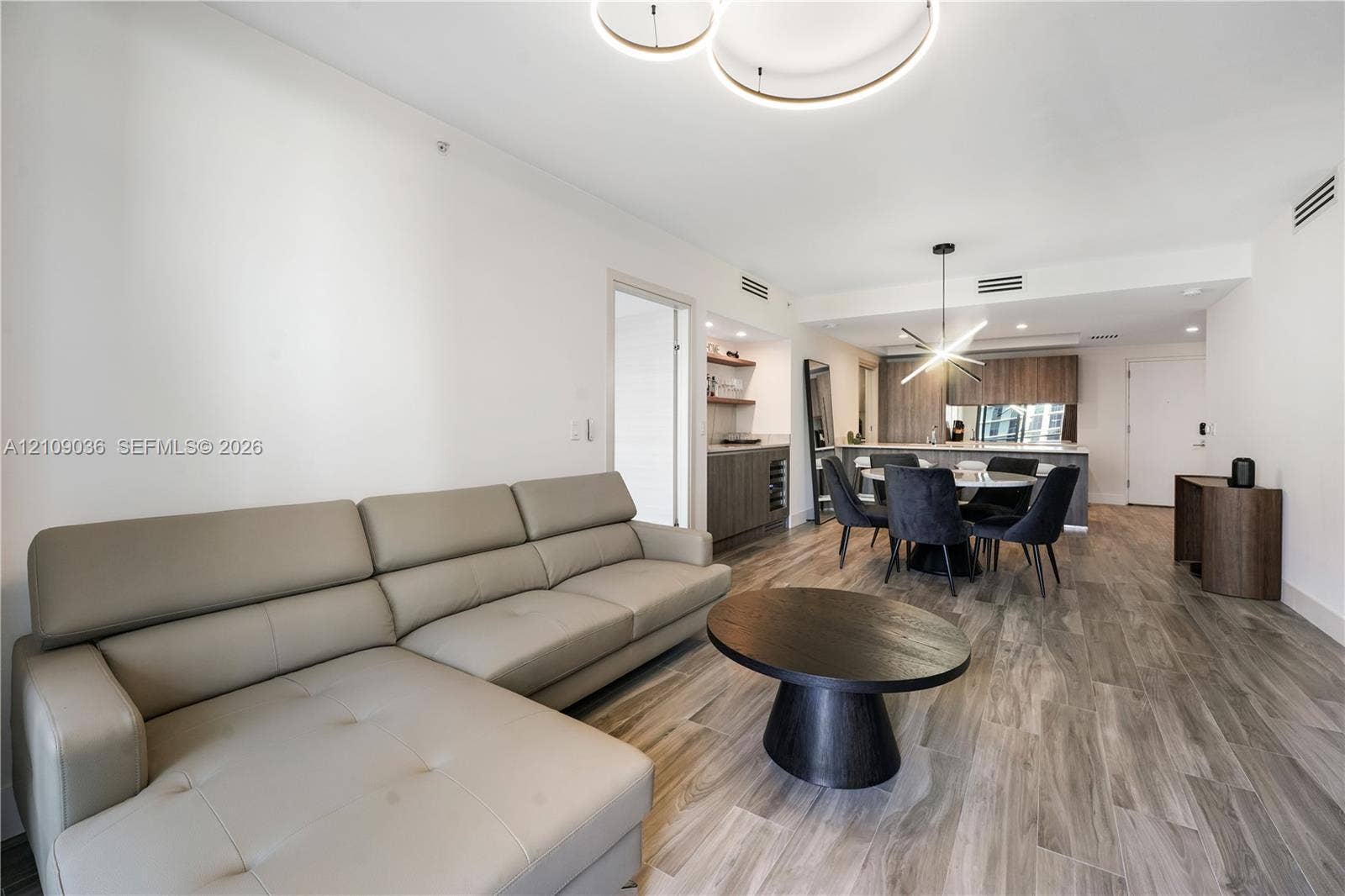 Open floor plan featuring wood-finish flooring, recessed lighting, modern circular halo chandelier, built-in wet bar with cabinetry, and kitchen with a central island