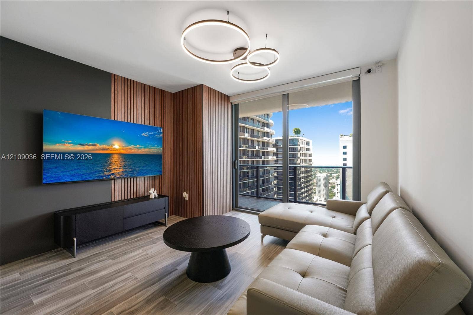 Living space featuring wood-finish flooring, floor-to-ceiling windows, modern multi-ring pendant lighting, and decorative wood-slat wall paneling