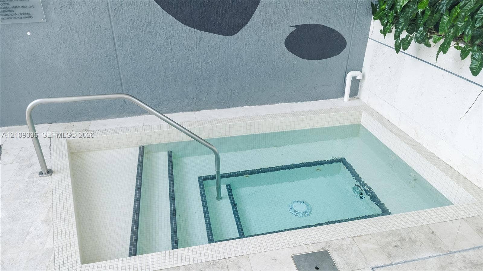 Inground plunge pool featuring white tile lining, multi-level stairs, stainless steel handrail, and stone tile surround
