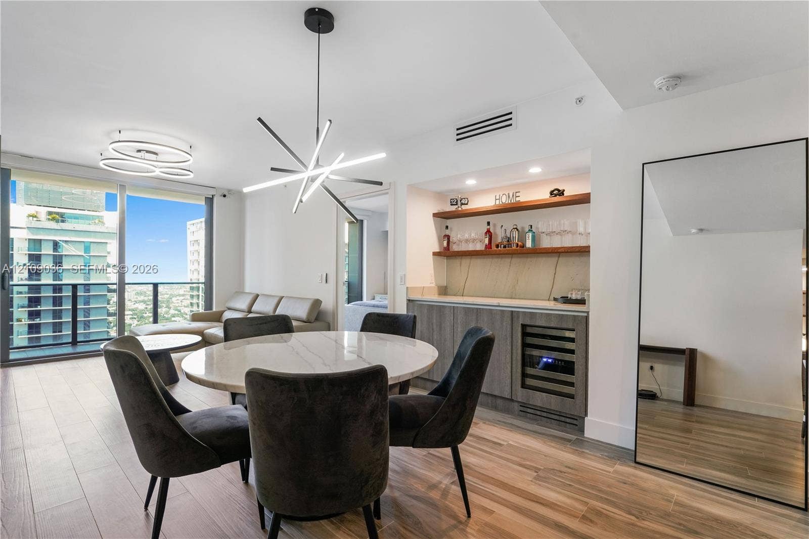 Built-in wet bar featuring stone-finish backsplash, custom cabinetry, integrated wine refrigerator, and wood shelving, complemented by wood-finish flooring and geometric pendant lighting