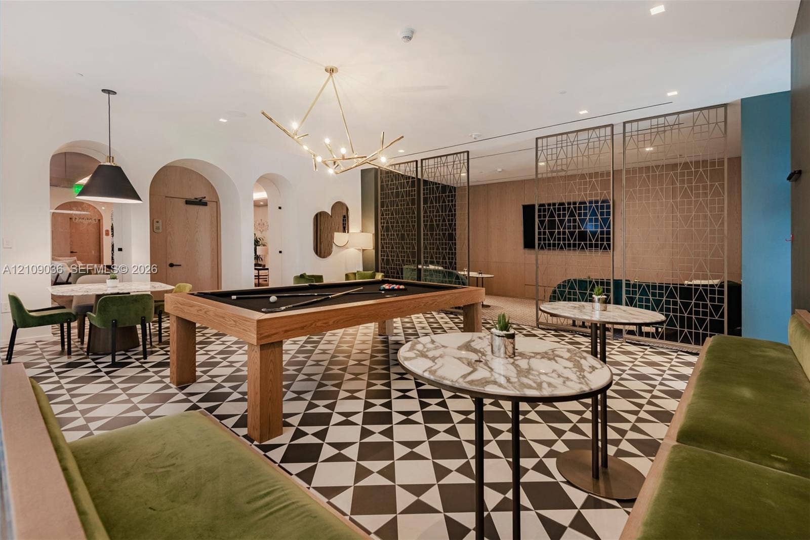 Geometric patterned tile flooring, arched wall openings, decorative metal privacy screens, wood-paneled accent wall, and multi-arm chandelier