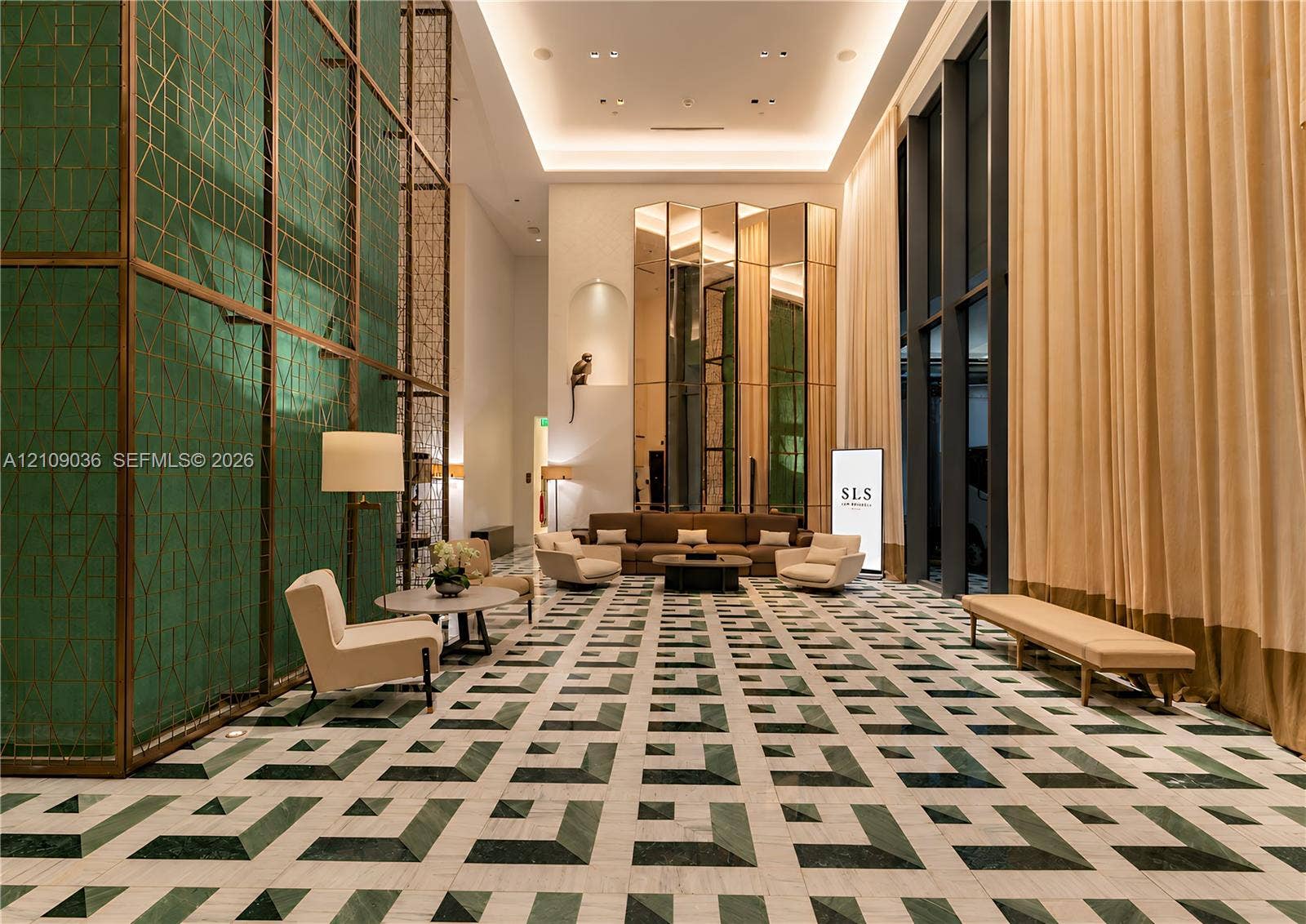 Grand lobby featuring double-height ceilings, intricate green geometric wall cladding, full-height window treatments, and patterned stone flooring
